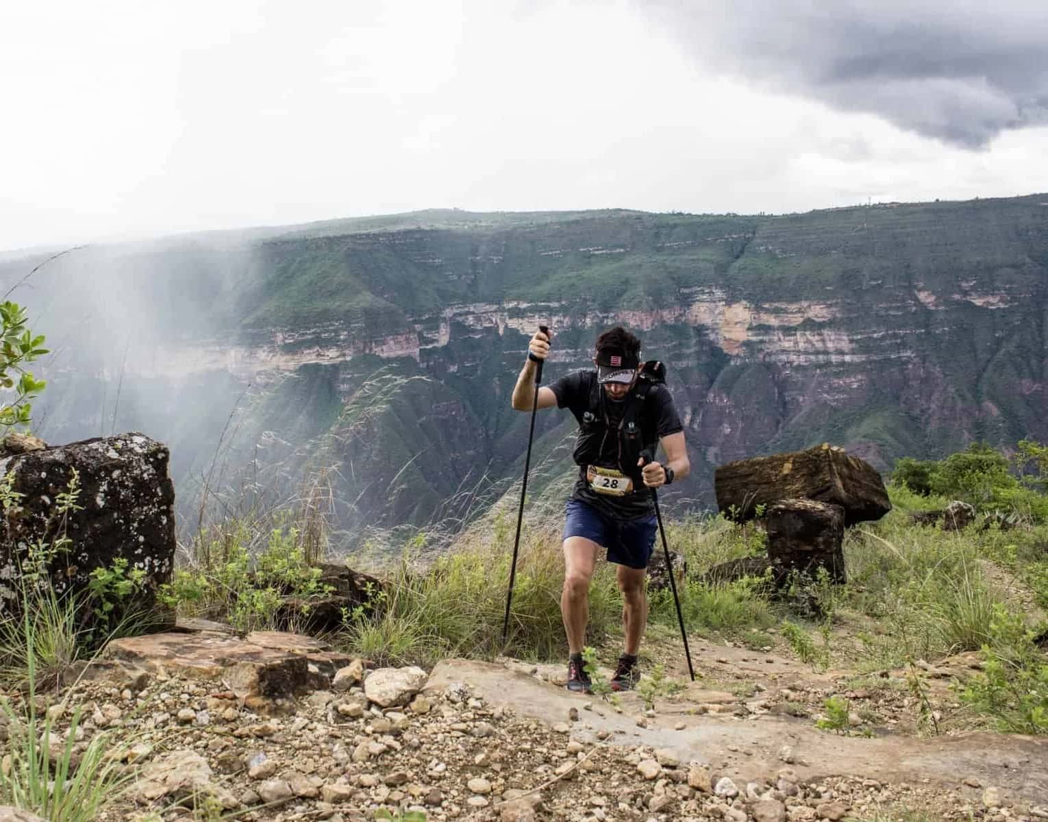 Runner with poles on the rim of the Chicamocha Canyon, with mist-covered canyon walls behind him