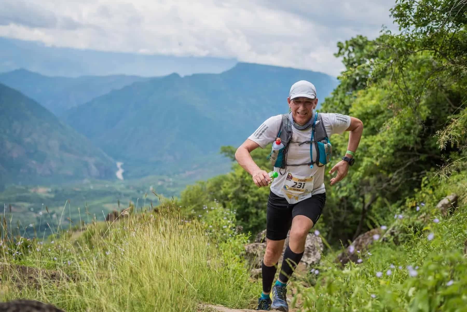 Smiling runner climbing a mountain trail with the valley behind