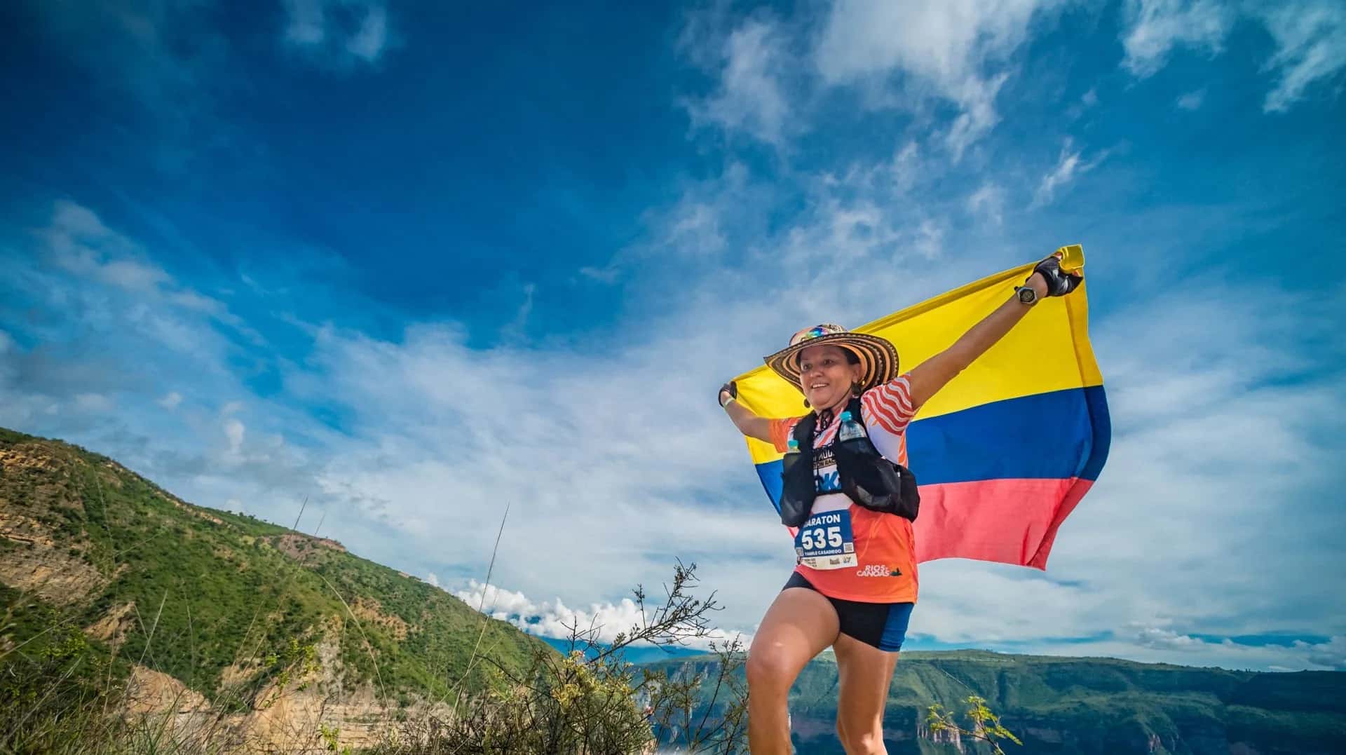 Runner holding the Colombian flag and wearing a sombrero vueltiao on the canyon rim