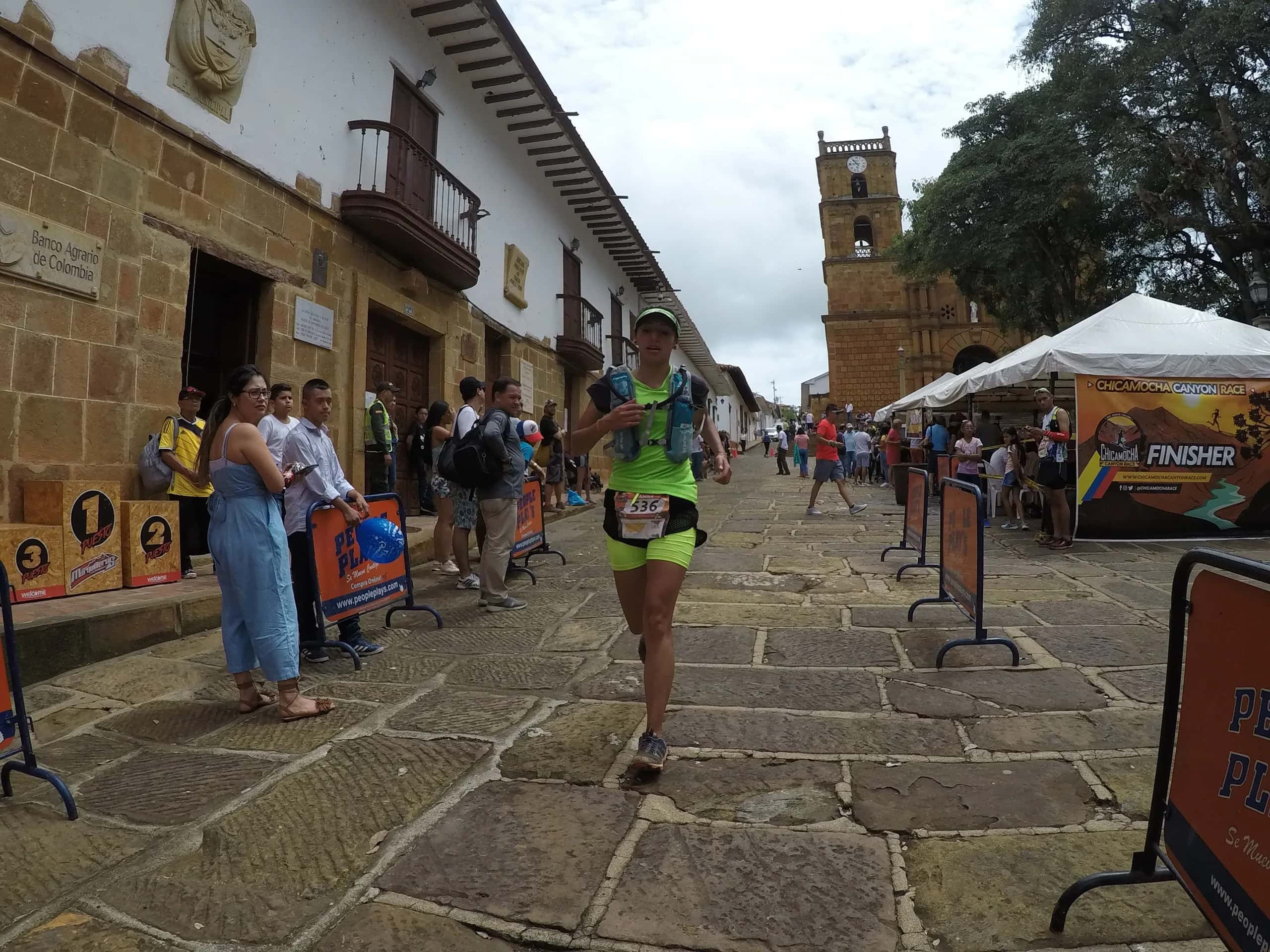 Corredora llega por la calle empedrada de Barichara, con el templo de piedra al fondo