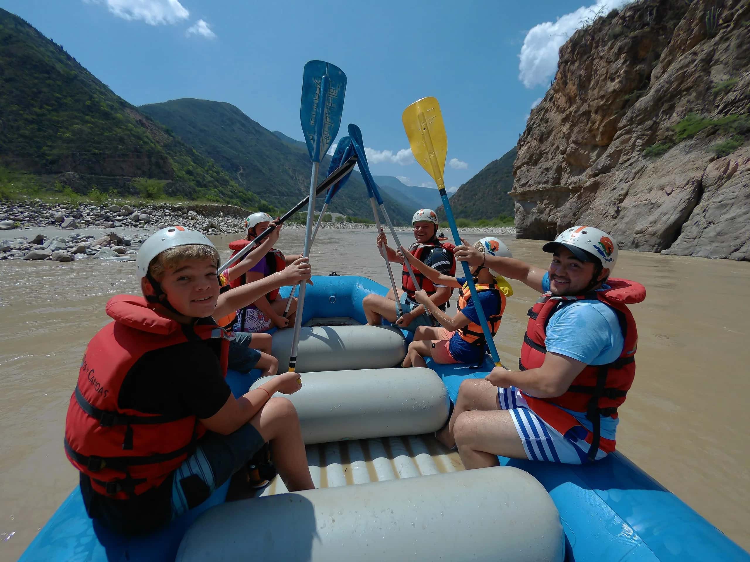 Family in a raft holding their paddles up on the river, between the canyon walls