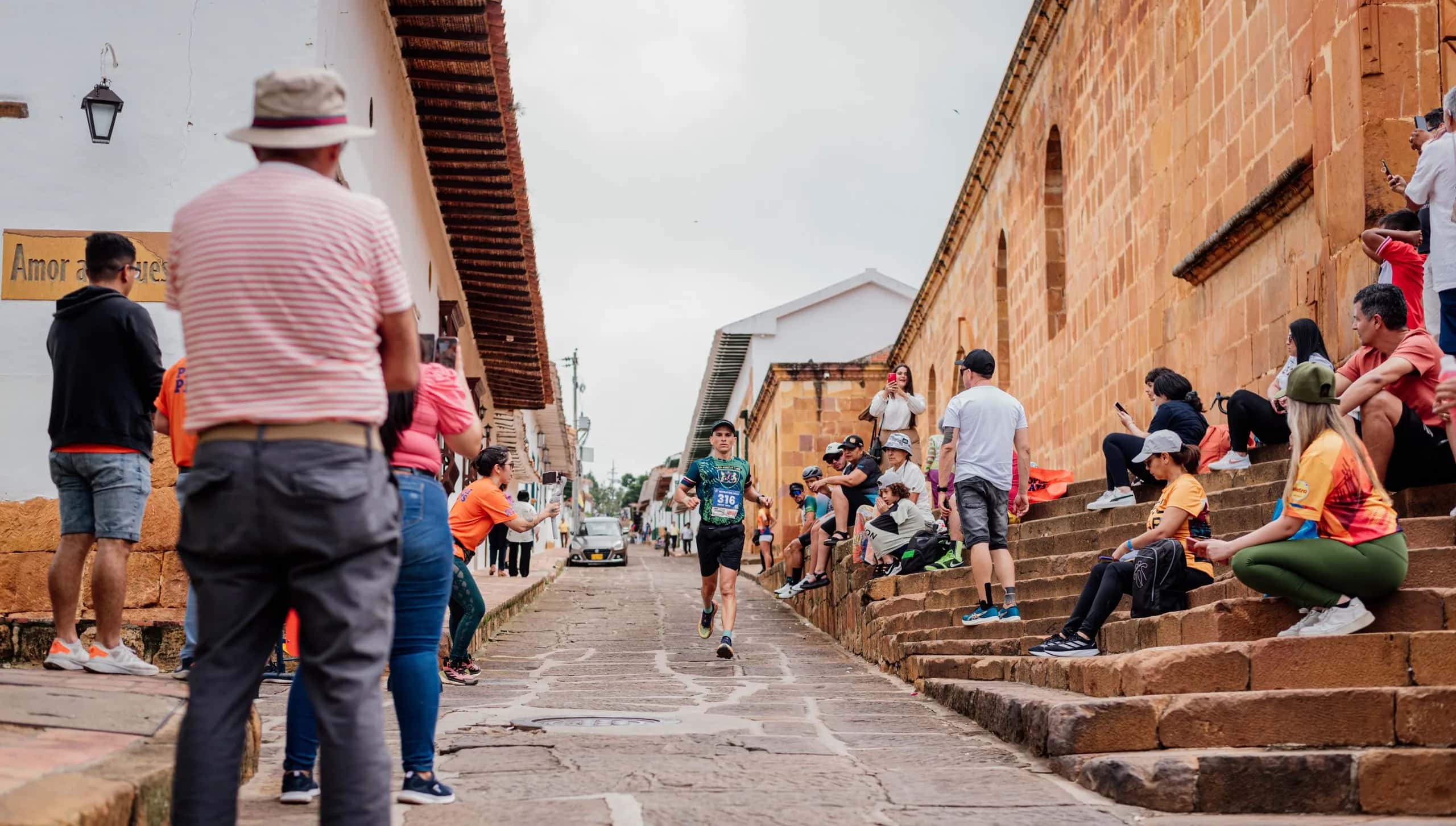 Runner makes his way along a cobbled colonial street as spectators cheer from the stone steps