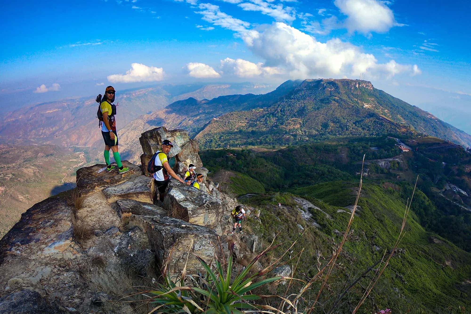Runners on a rocky summit above the canyon, with a large plateau and blue sky behind them