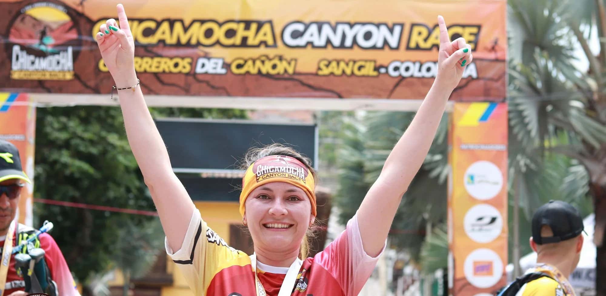 Runner celebrating with arms raised and her medal under the finish arch