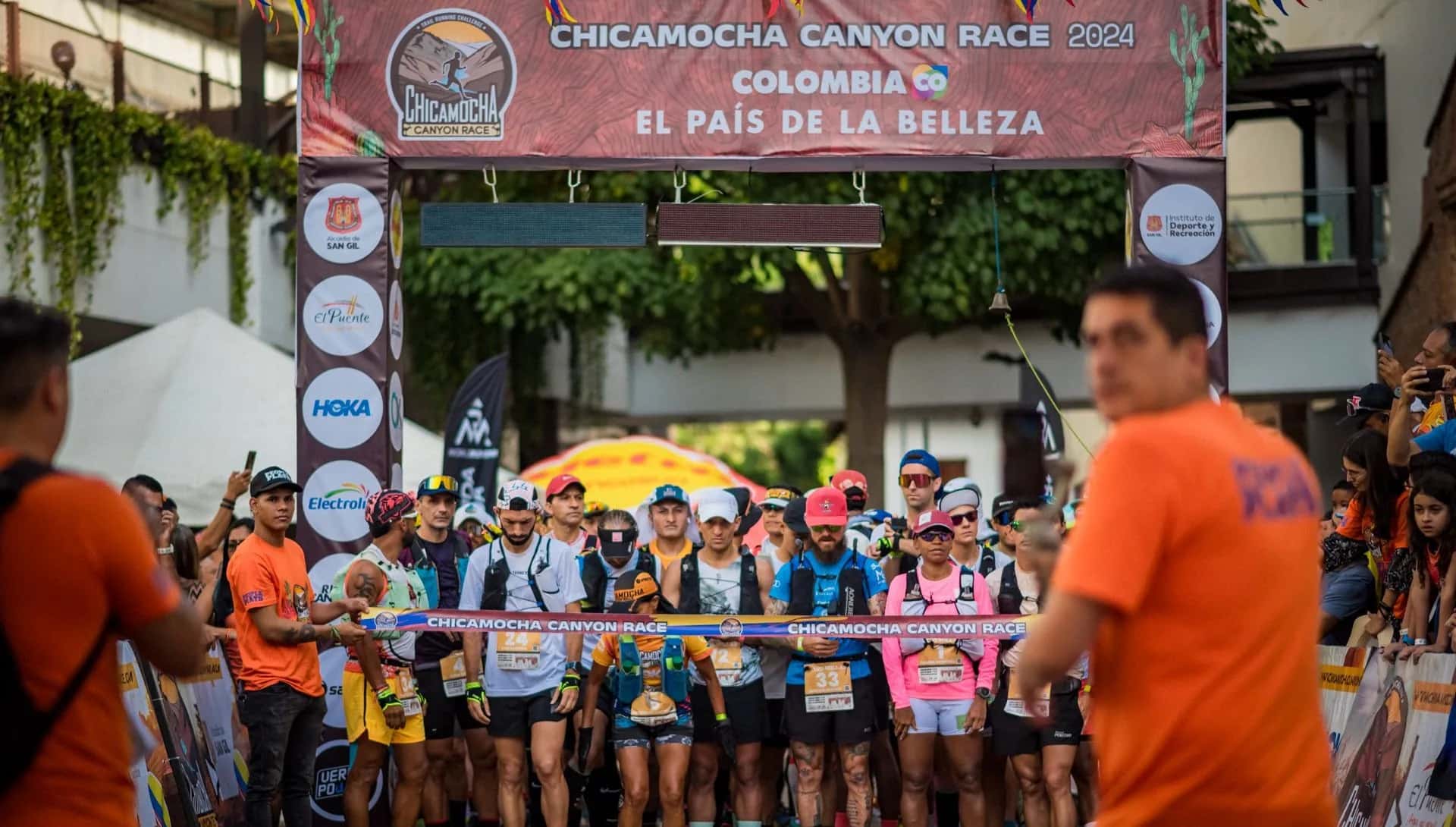 Runners on the start line under the Chicamocha Canyon Race gantry, with spectators on both sides