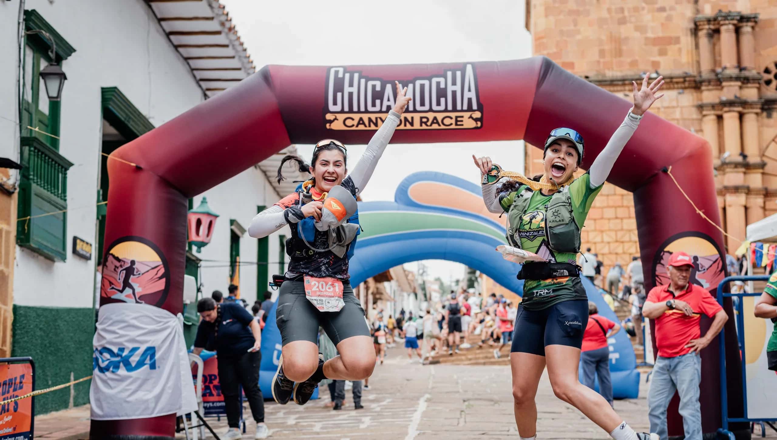 Two runners jumping for joy as they cross the finish arch on a colonial street