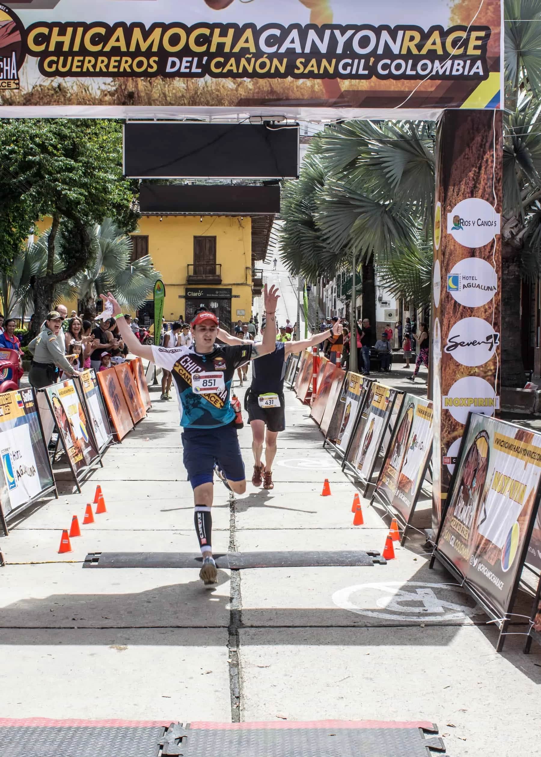 Runner crossing the finish with open arms along the barrier-lined chute