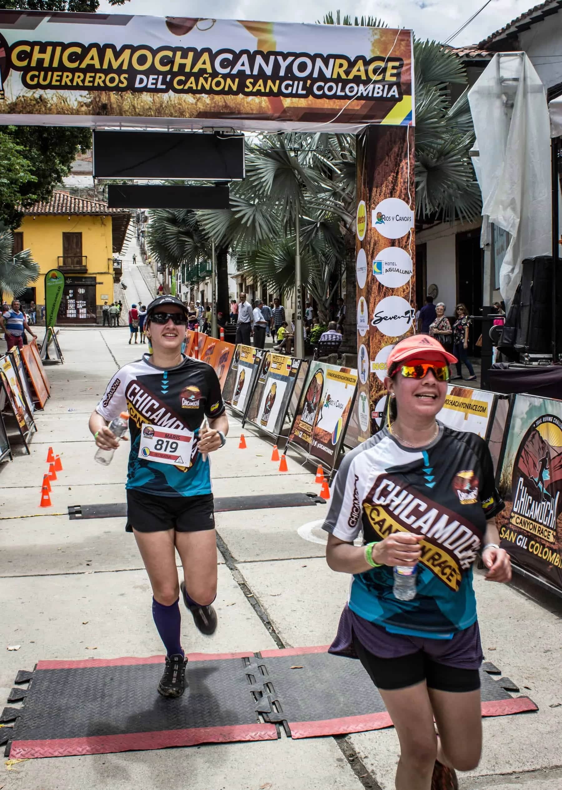 Two smiling runners step onto the finish mat under the finish gantry