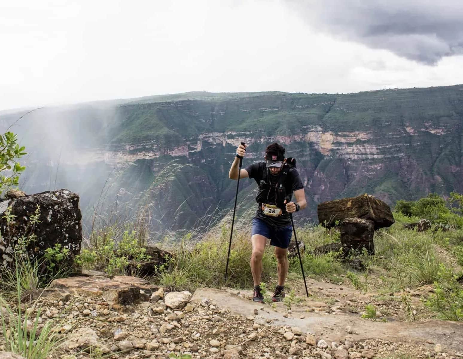 Runner with poles on the canyon edge, with mist over the rock walls