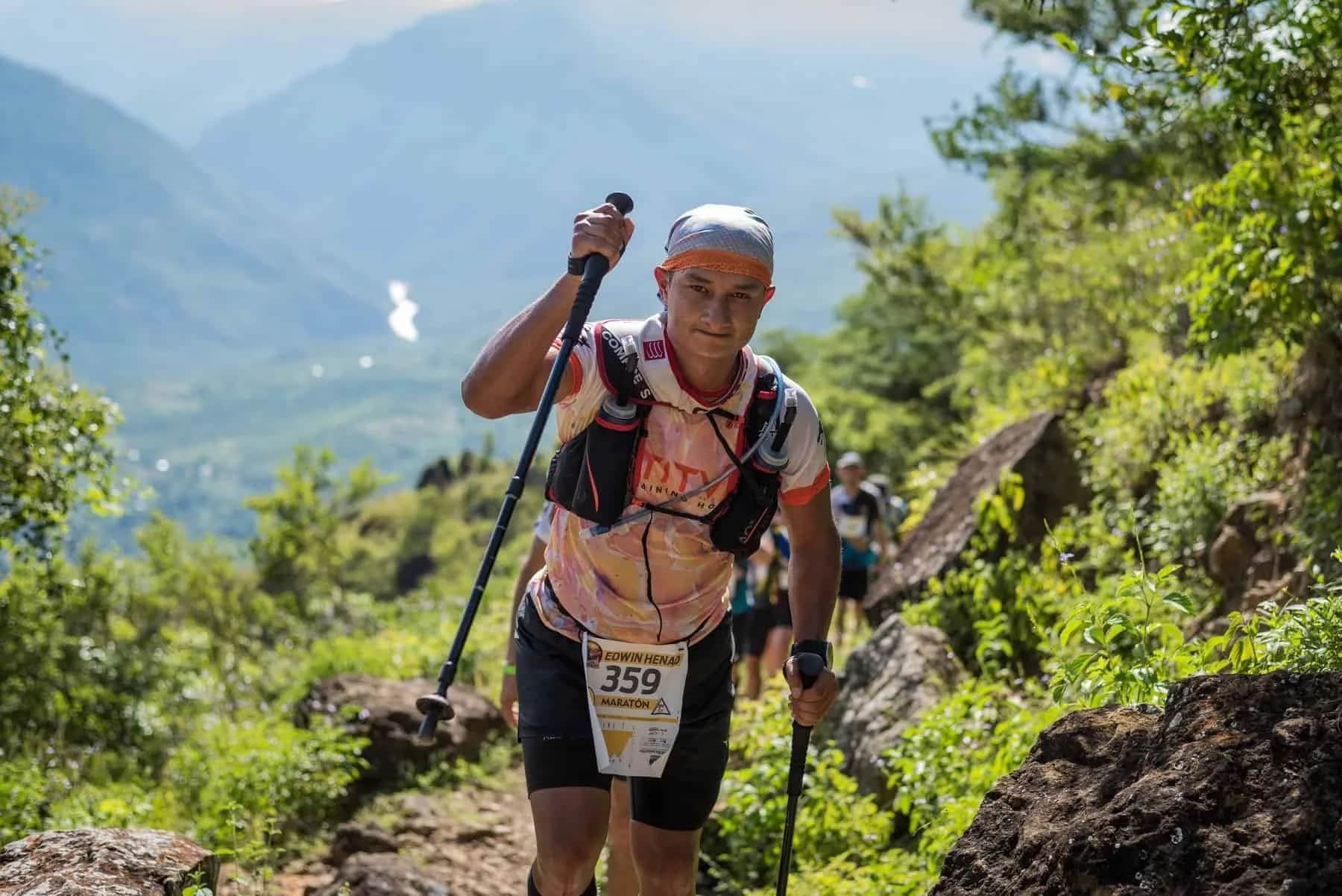 Smiling runner with poles climbing a rocky trail among trees
