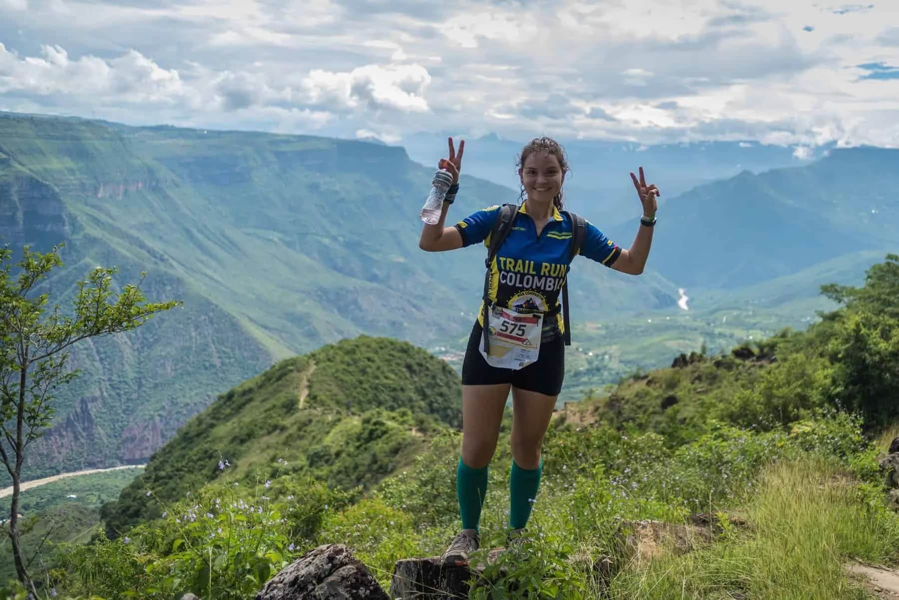 Runner making the peace sign on a trail with the canyon and river behind