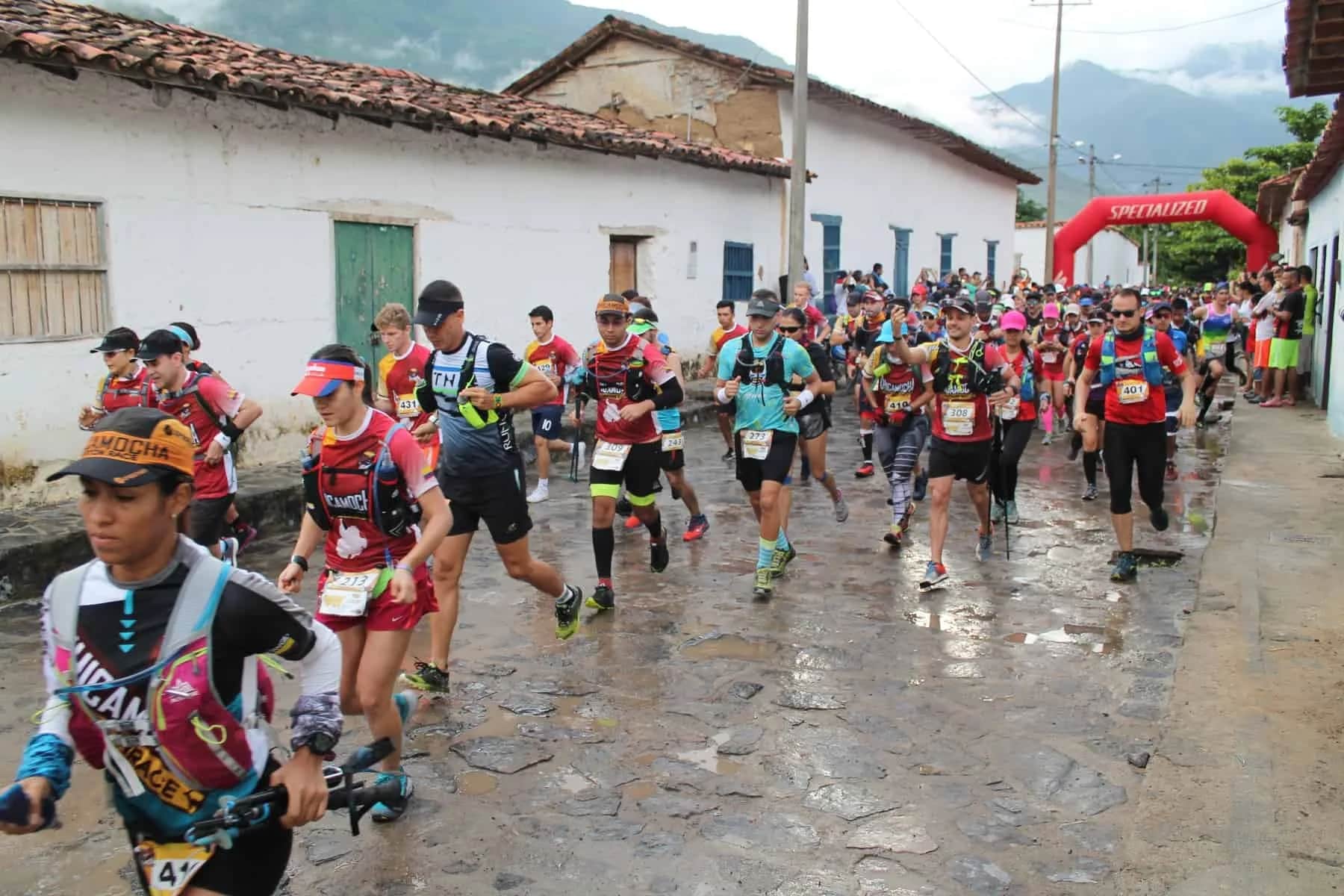 A pack of runners on a wet cobbled street lined with white houses