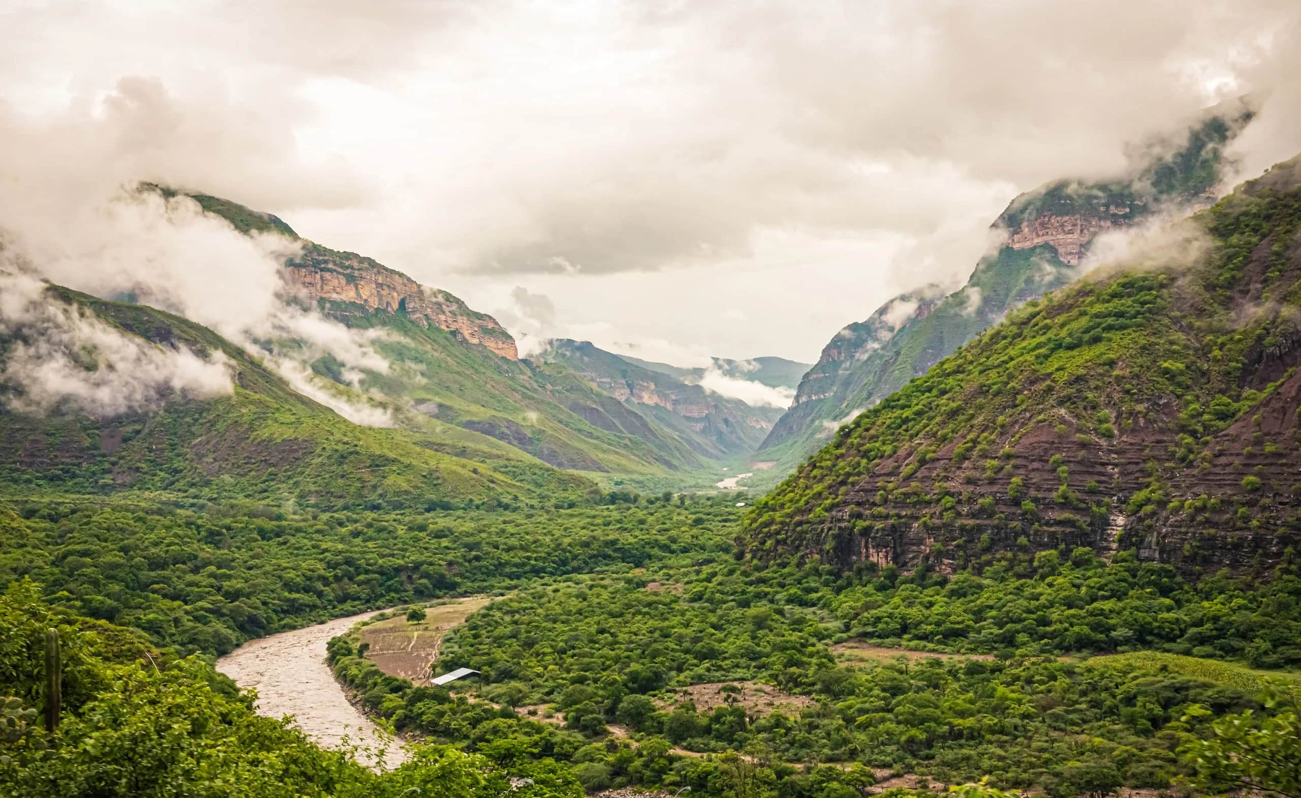 The Chicamocha River winding between green slopes, with clouds over the canyon walls