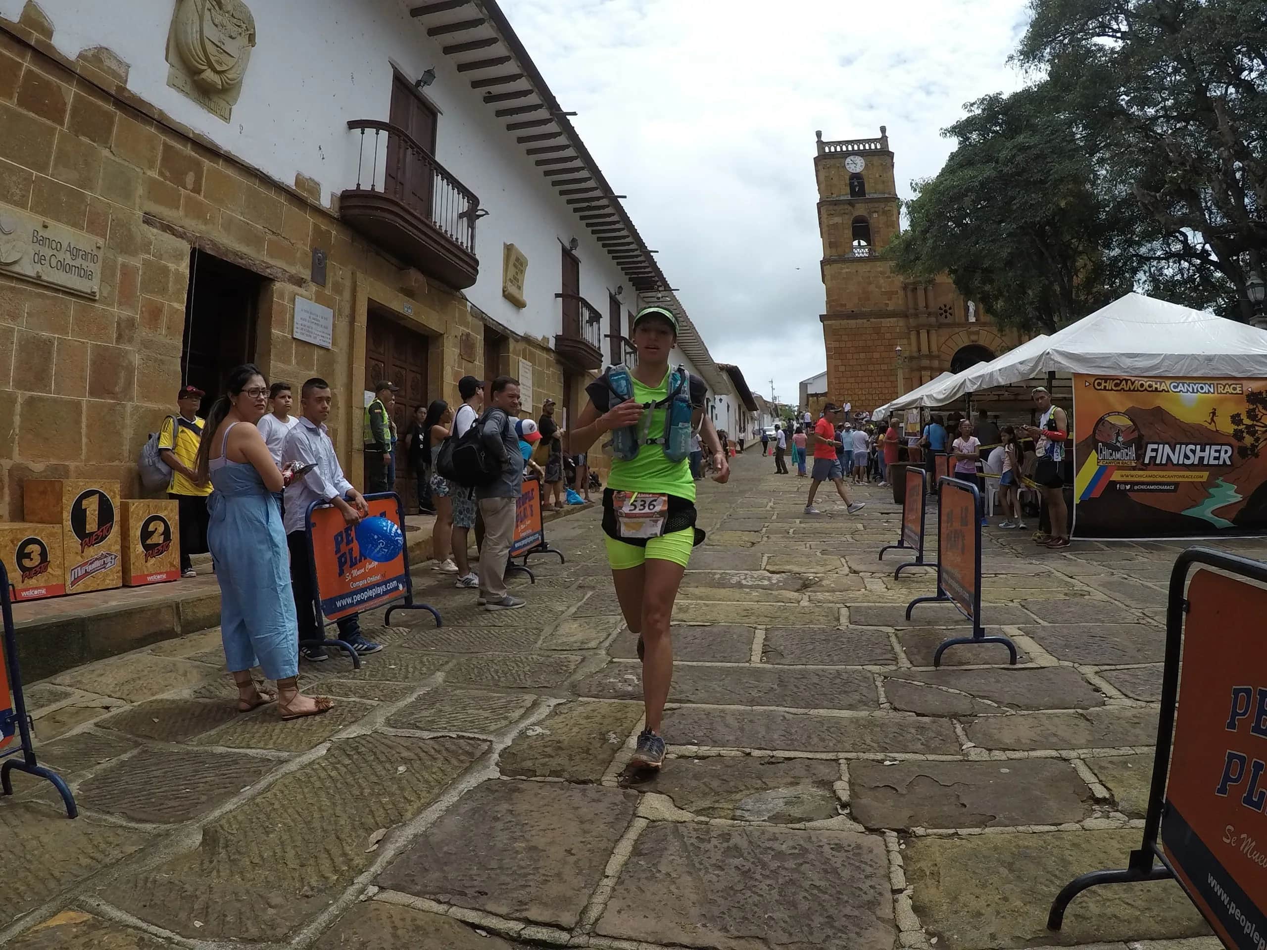 Runner arriving along a cobbled street in Barichara, with the stone church behind