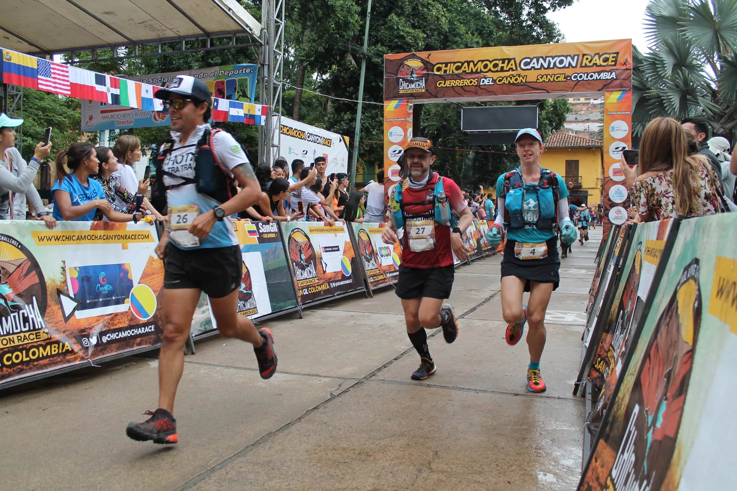 Runners come down the finish chute between barriers, flags and spectators