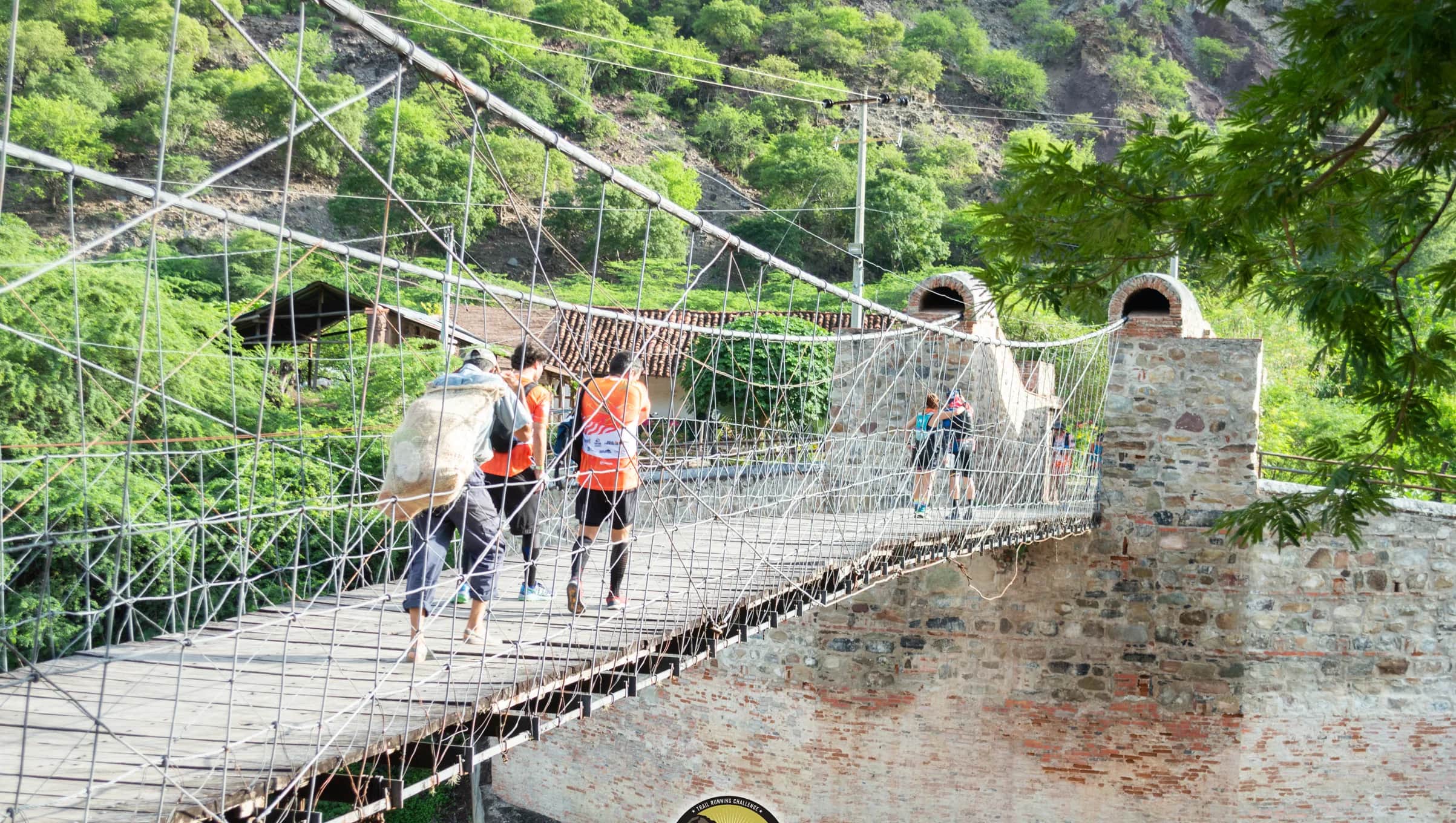 Runners crossing a wood-and-cable suspension bridge over the river