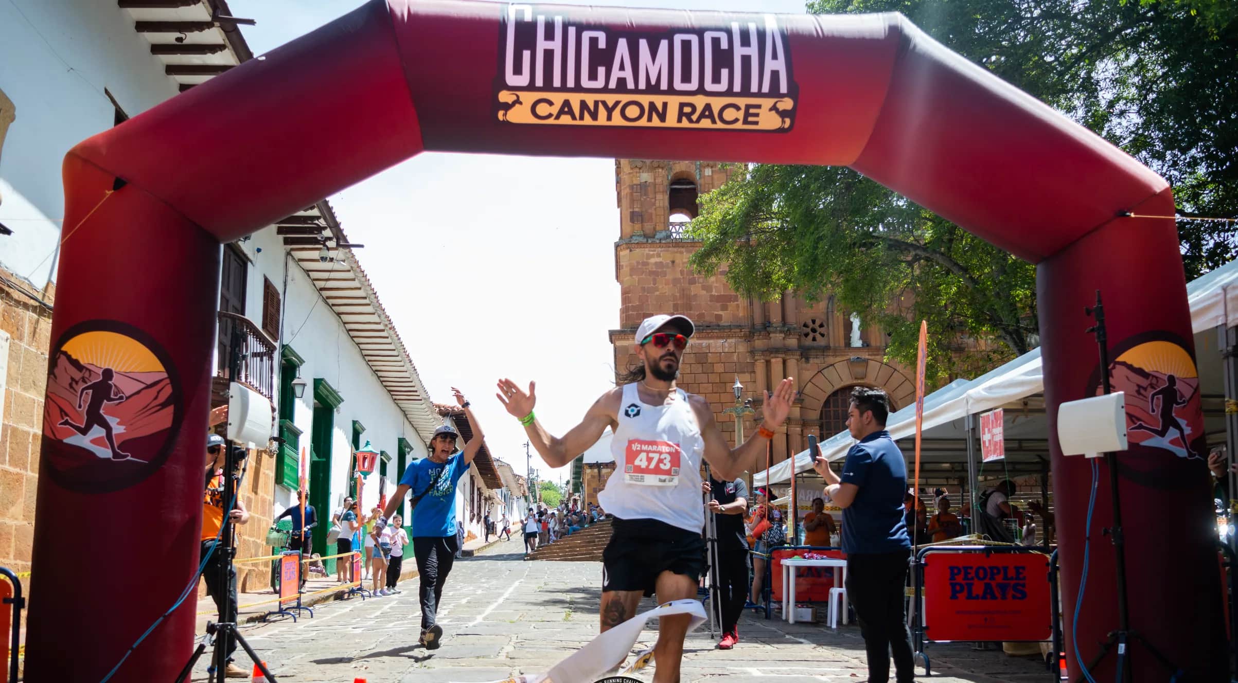 Runner breaking the finish tape in front of a colonial village church