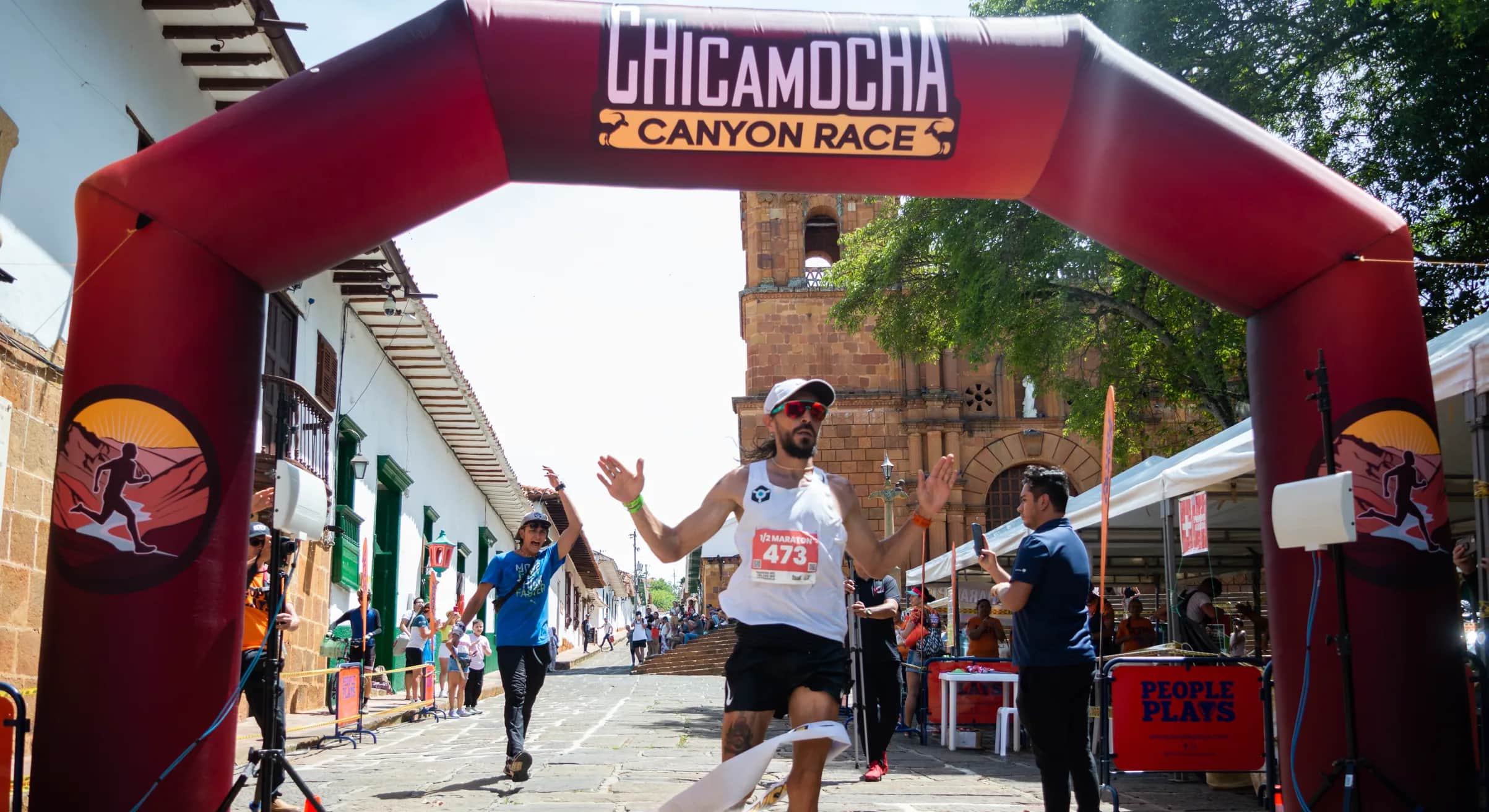 Runner breaks the tape under the finish arch on a cobbled street
