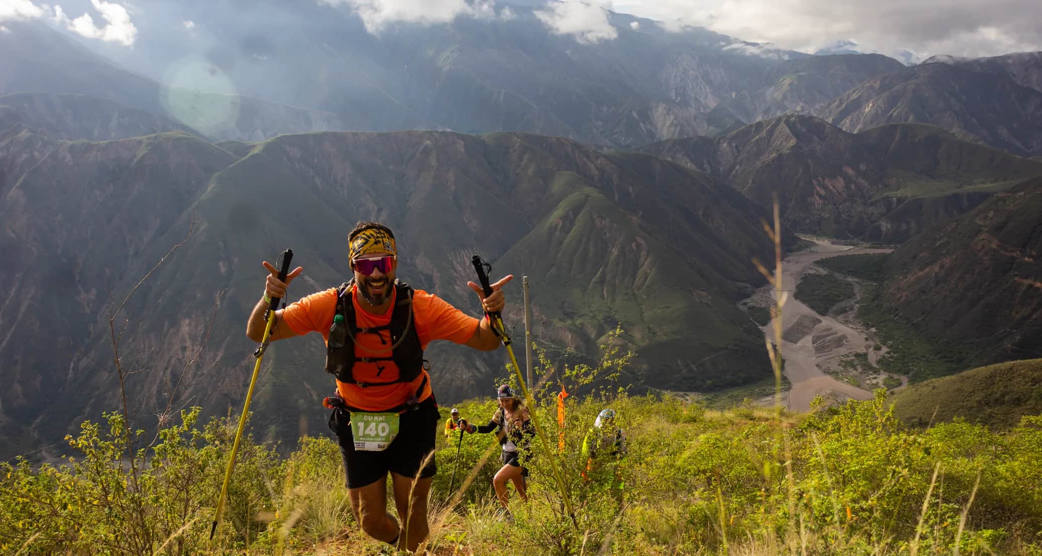 Runner raising his poles in celebration on a grassy slope, with the canyon behind