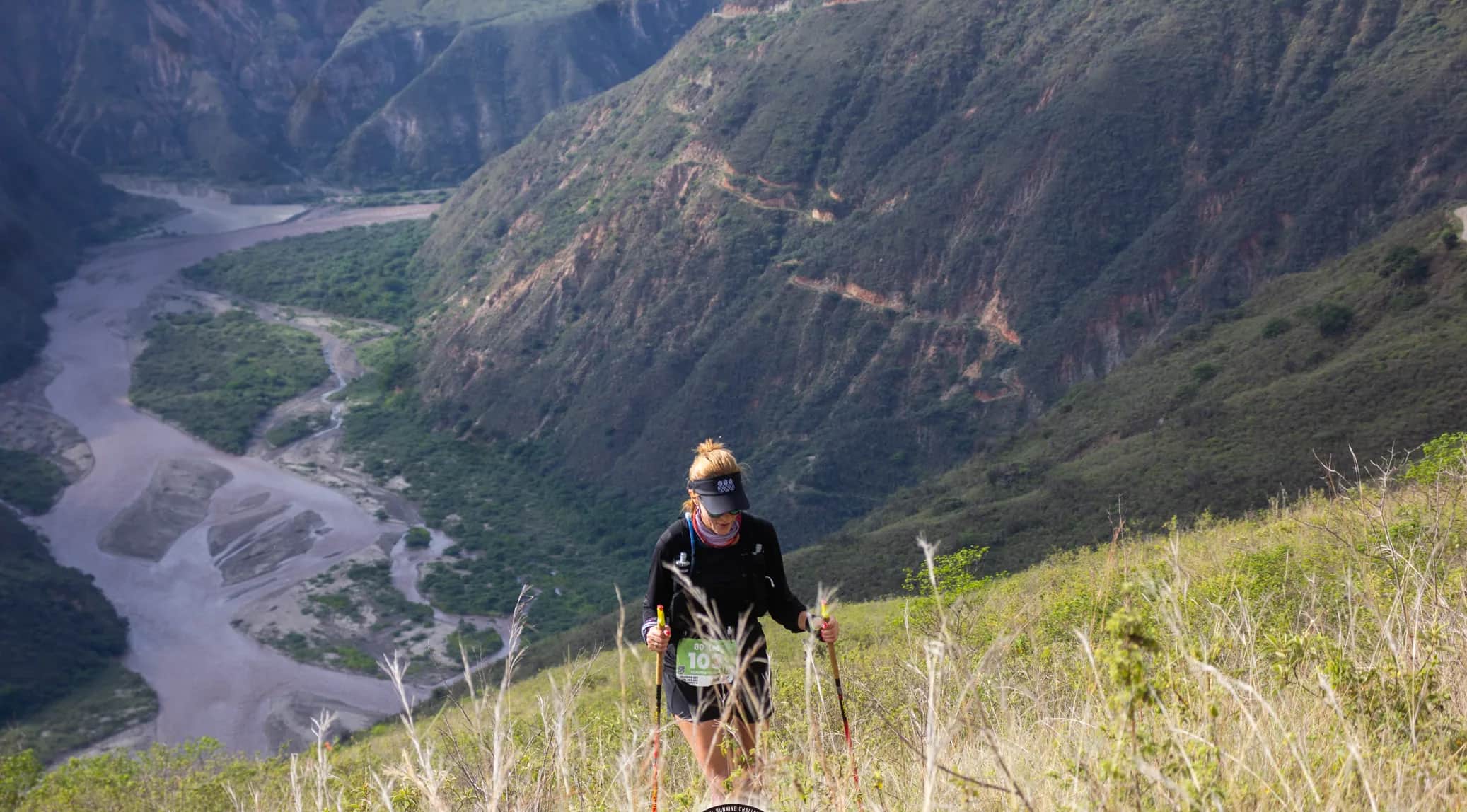 Runner with poles on a grassy slope above the canyon river