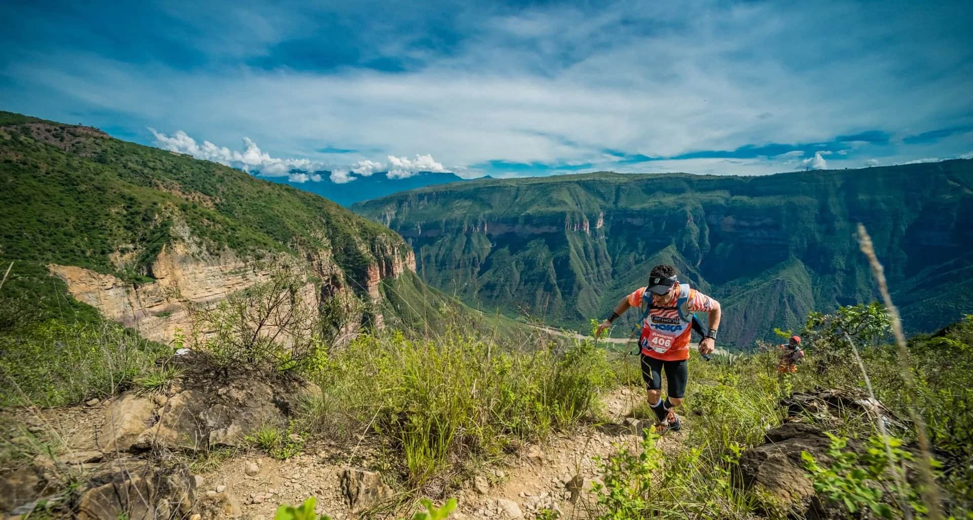 Runner climbing a grassy trail with the canyon walls behind