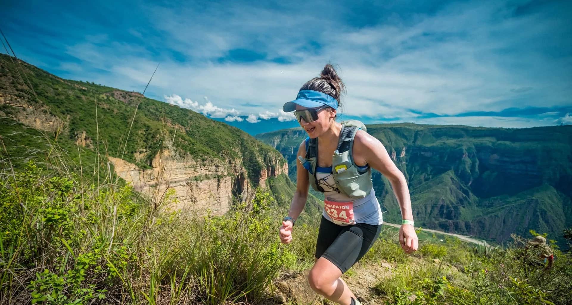 Runner moving along the canyon rim with the rock walls and valley behind her