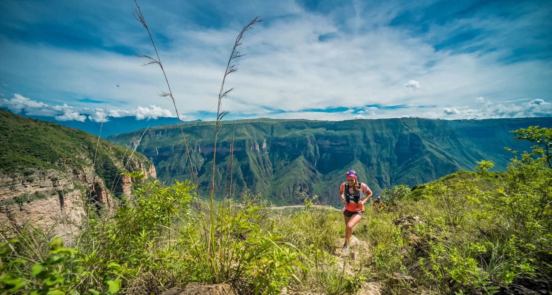 Runner climbing toward the canyon rim with the plateau and blue sky behind