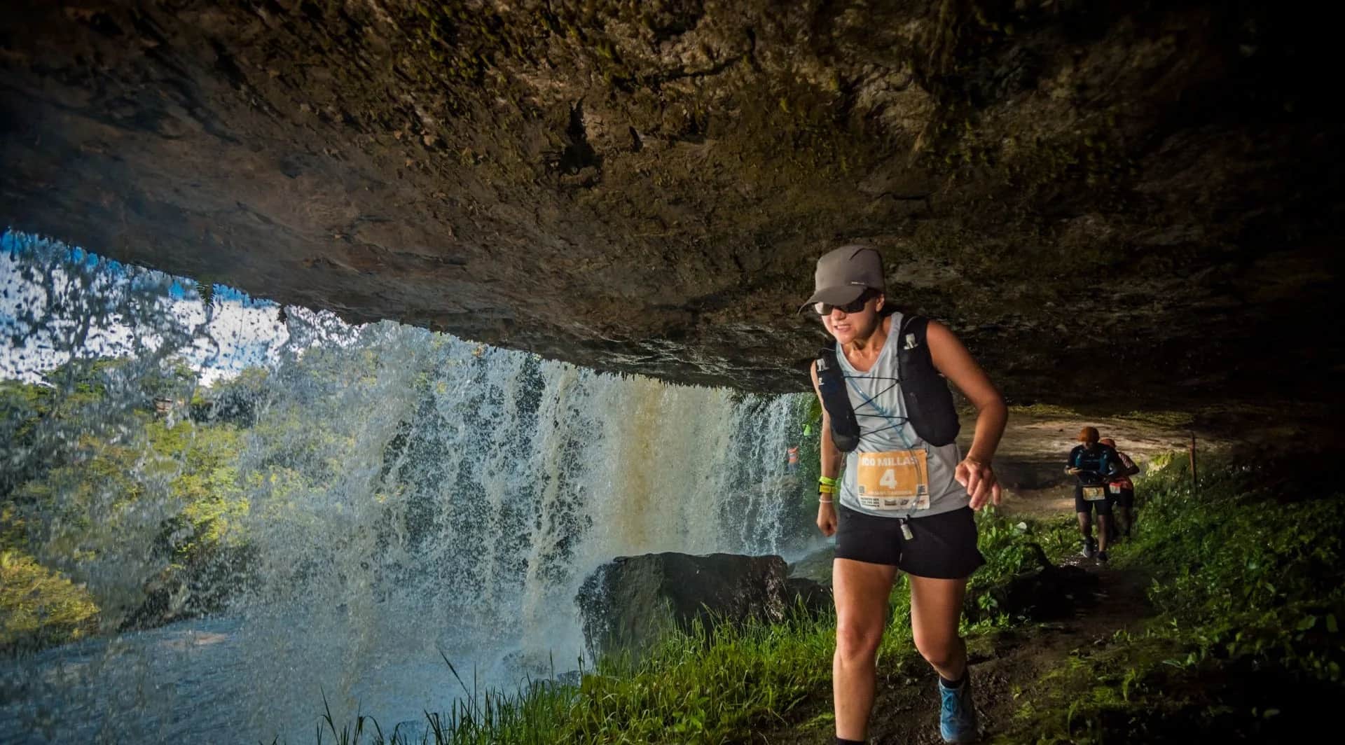 Runner passing behind a waterfall under a rock overhang