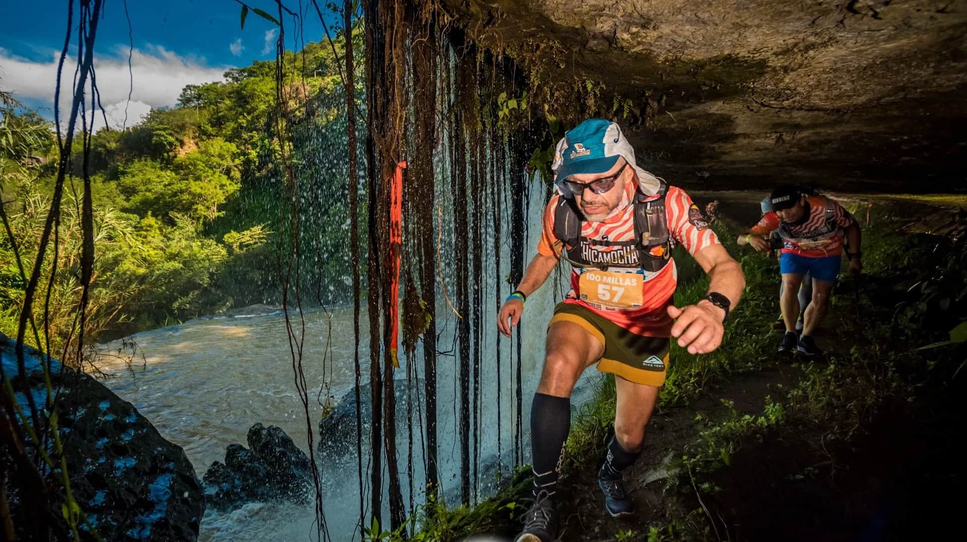 Runner passing under a curtain of roots beside a waterfall