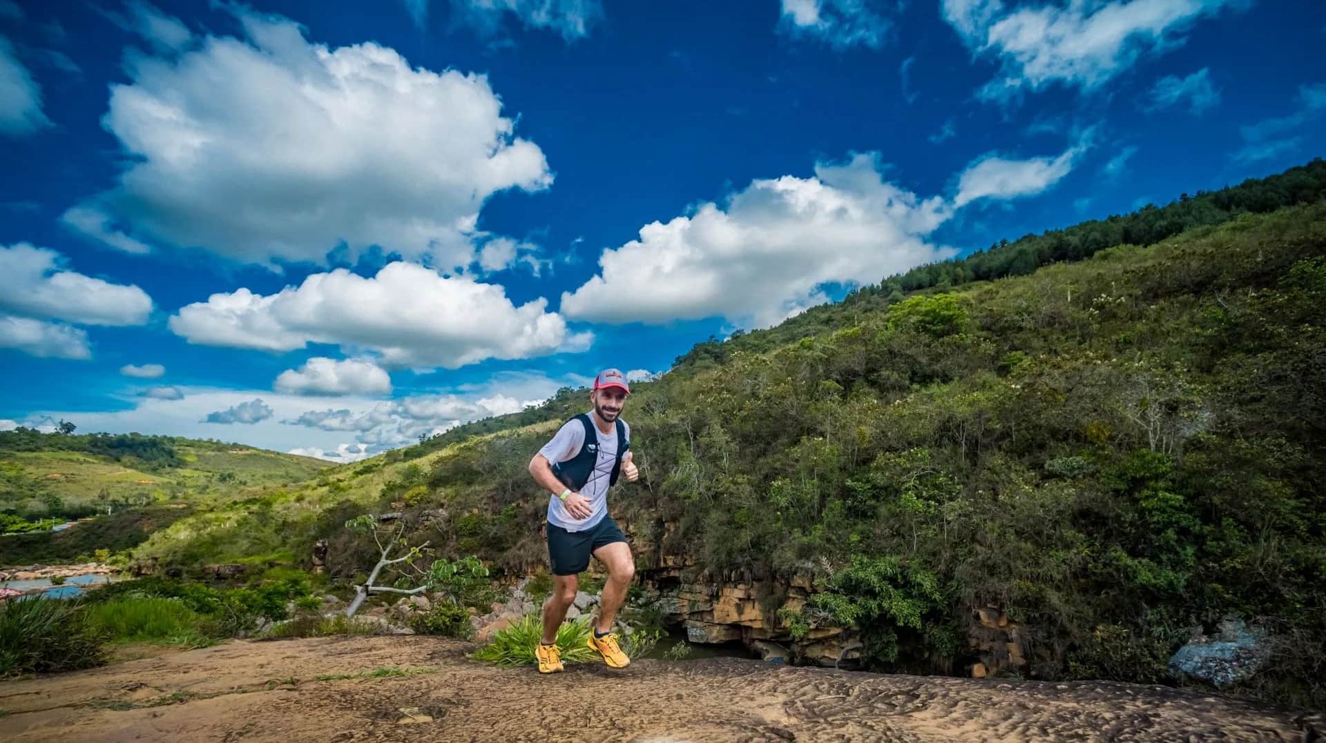 Runner crossing a rocky flat beside a river under a blue sky with clouds