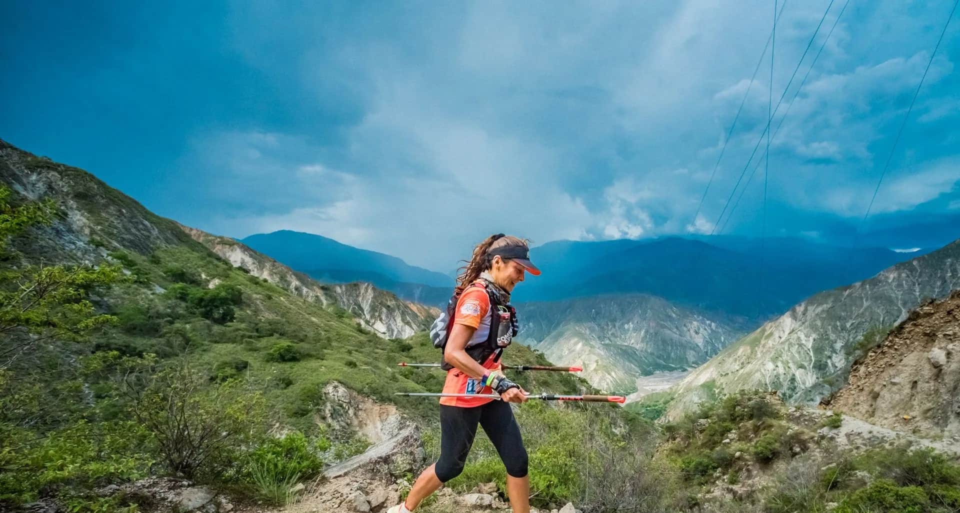 Runner with poles on a hillside trail, with the canyon and clouds behind