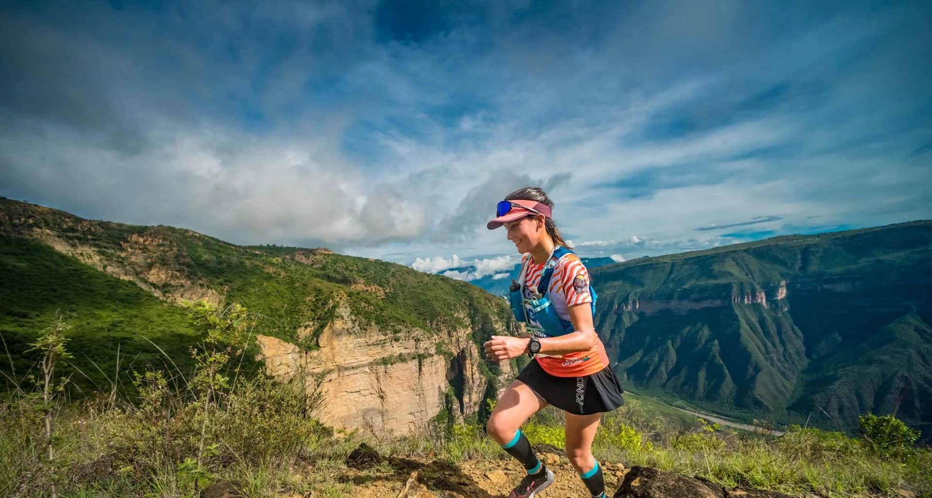 Runner climbing between rocks with the canyon and a cloudy sky behind