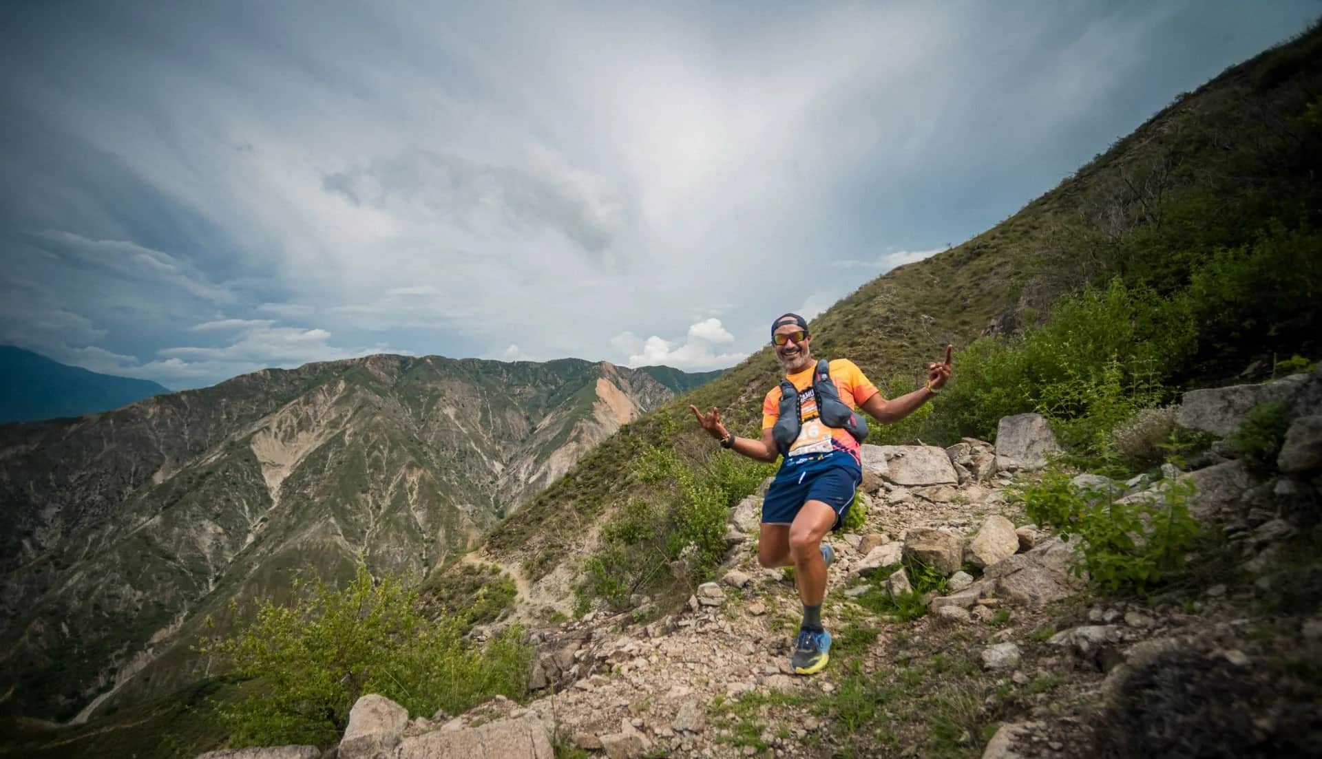 Runner celebrating on a rocky descent under a dramatic sky over the canyon