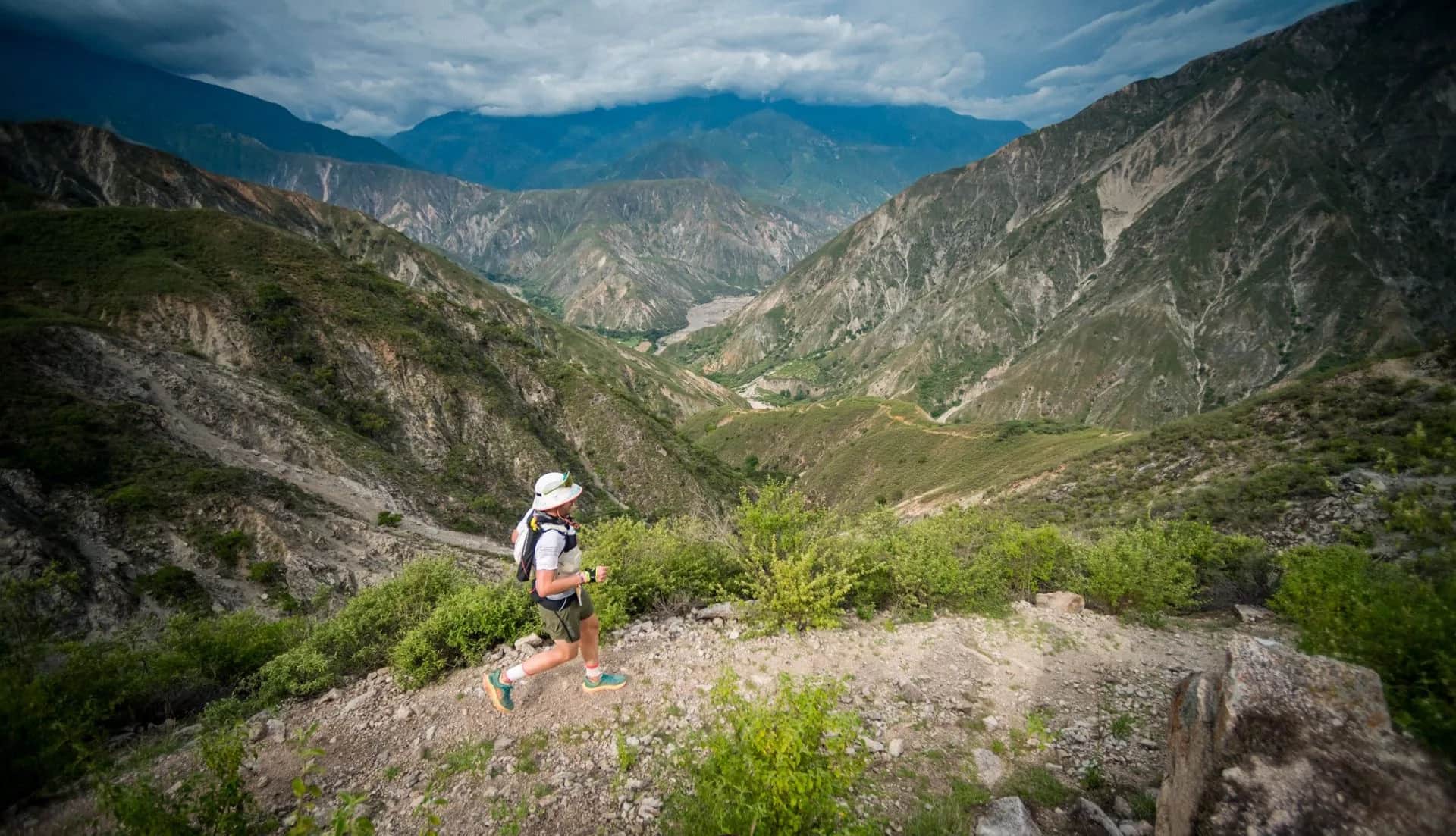 Runner on a stony trail facing the deep canyon, with the river at the bottom of the valley