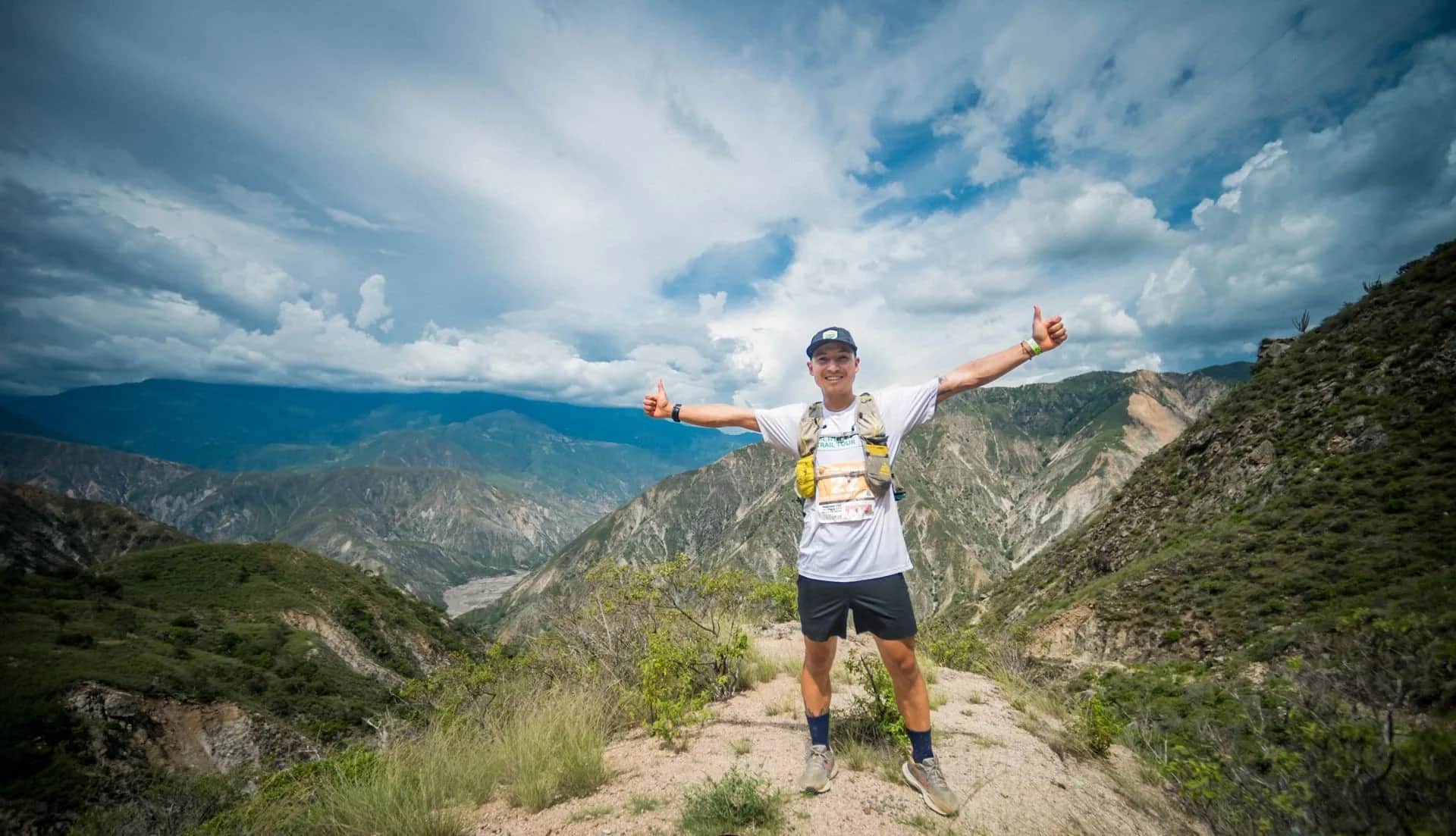 Runner with arms wide open at the top of a trail, the canyon under a cloudy sky