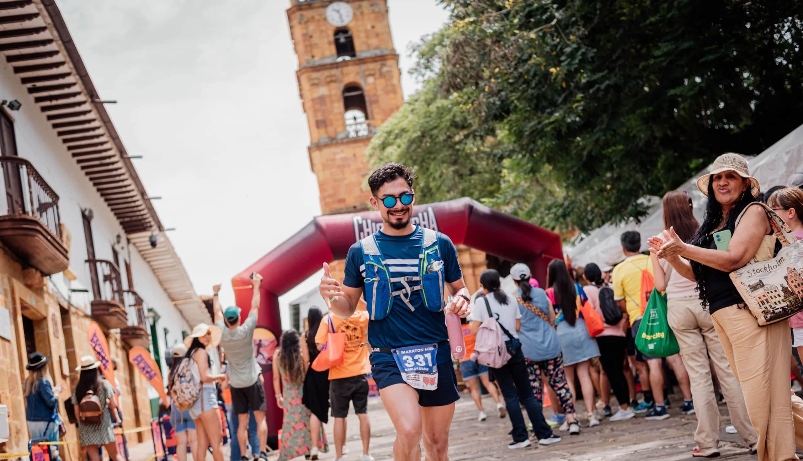Runner passing under the Chicamocha Canyon Race arch in Barichara, among spectators in front of the stone church