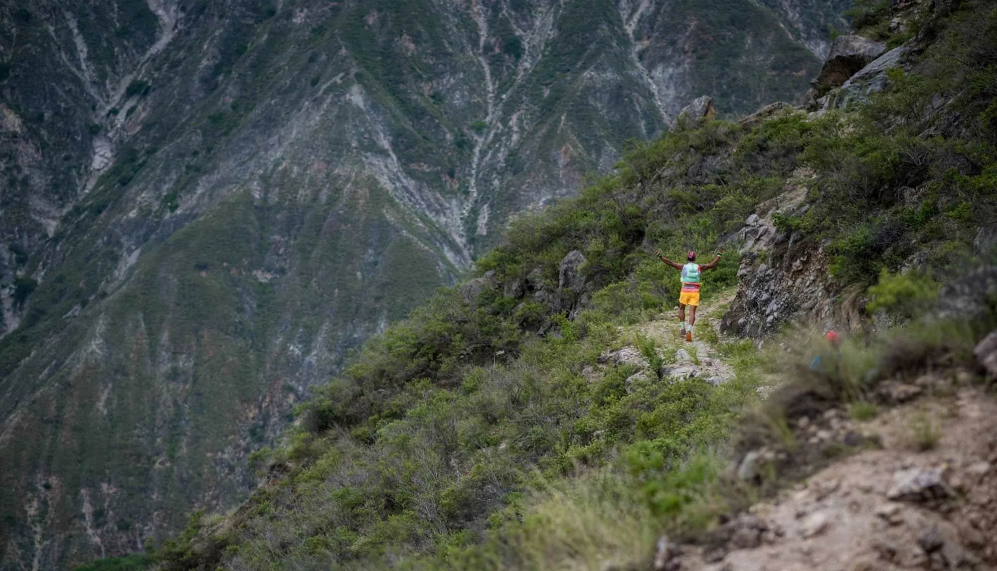 A tiny runner on a hillside trail against the canyon walls