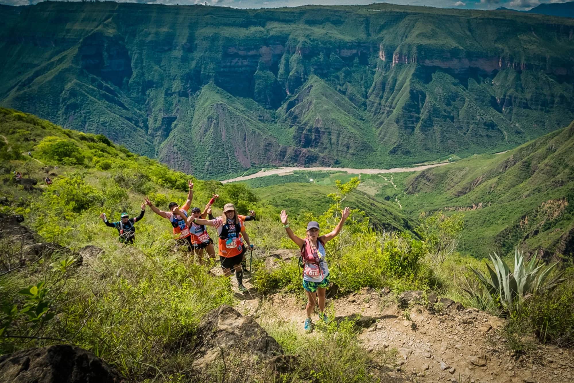 Group of runners waving from a trail with the canyon river below