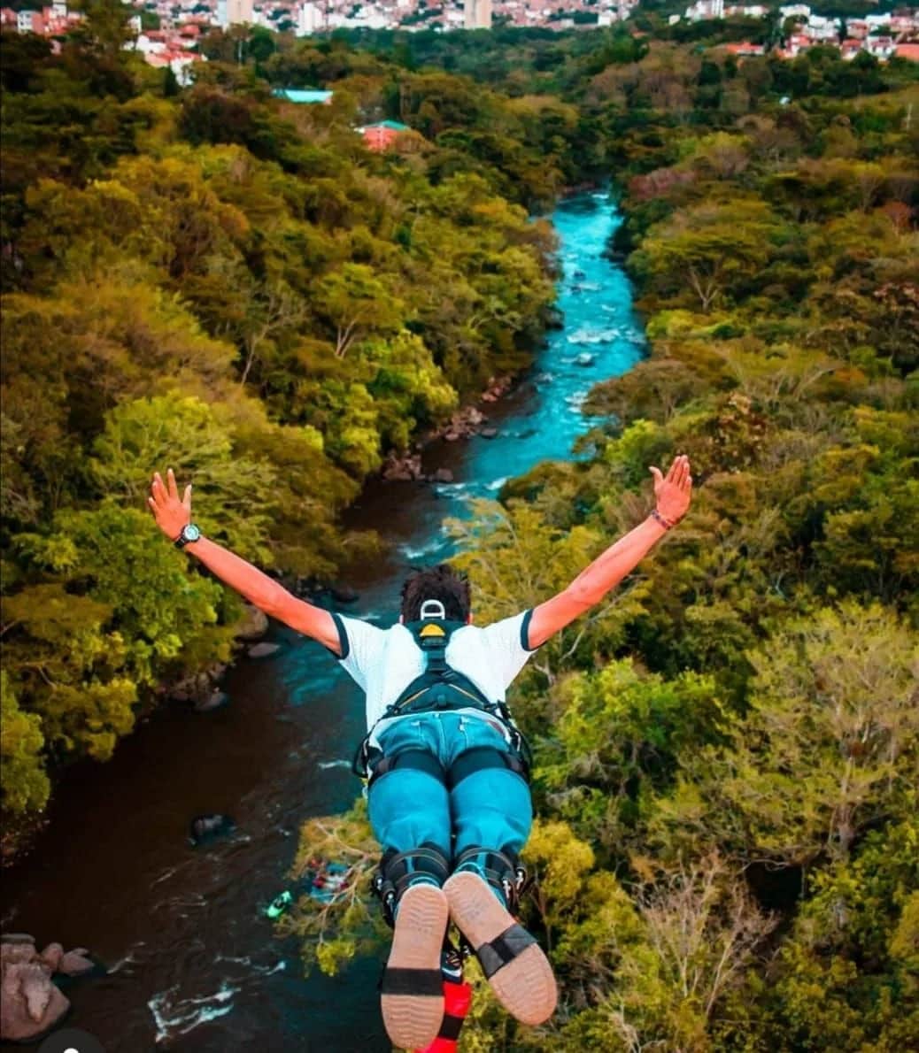 Person bungee jumping above a turquoise river surrounded by forest