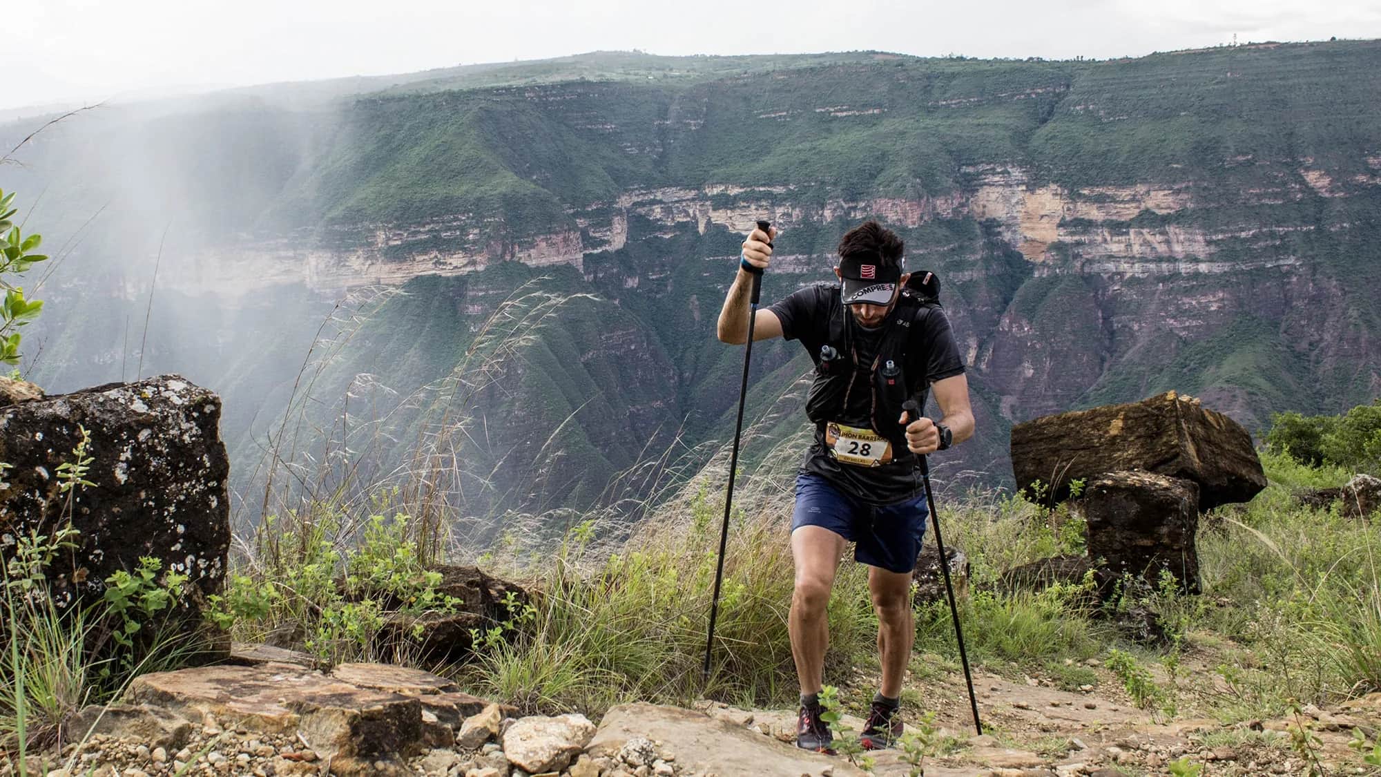 Runner with poles climbing between rocks as mist rolls over the canyon walls