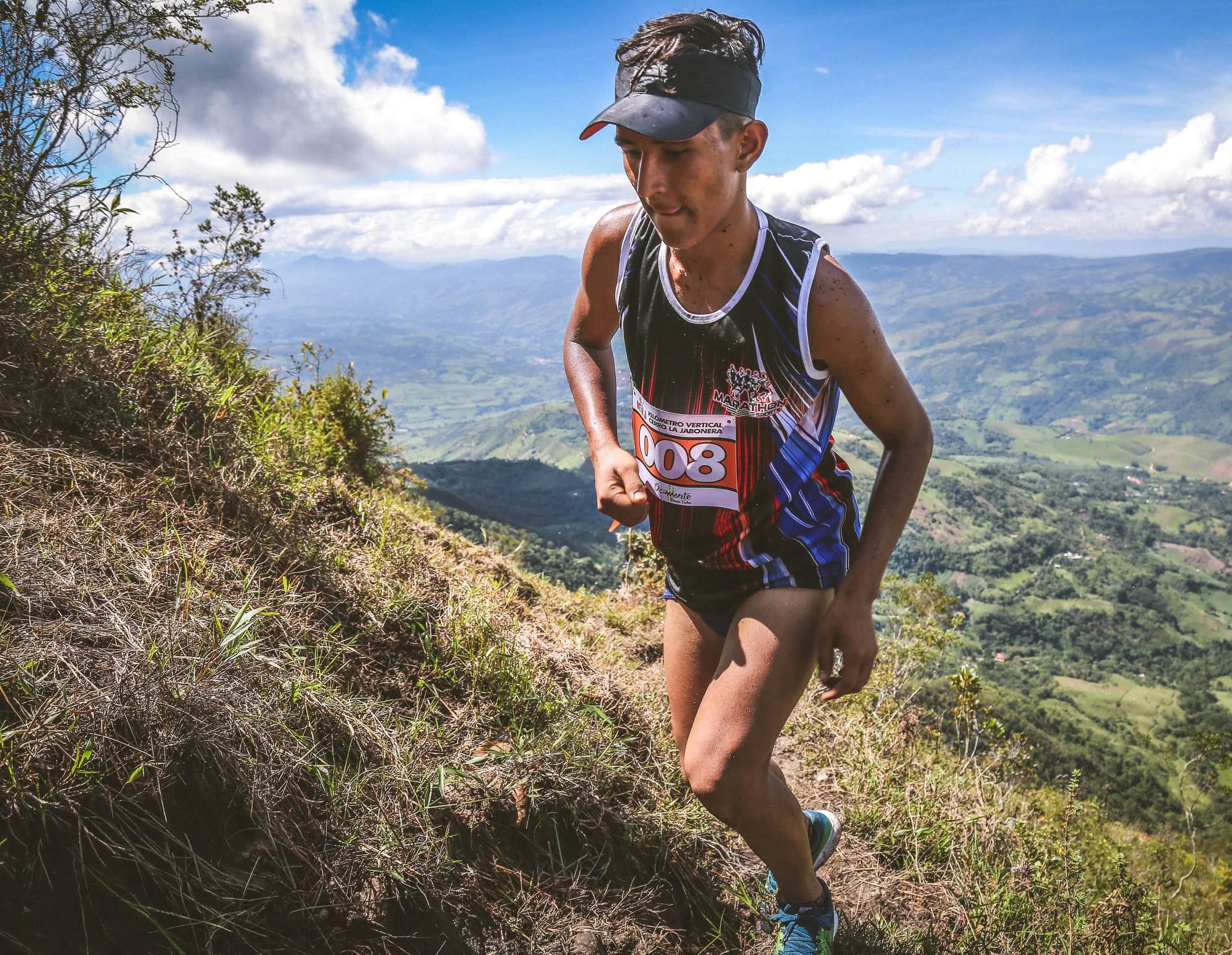 Runner climbing a grassy slope with the valley and mountains behind