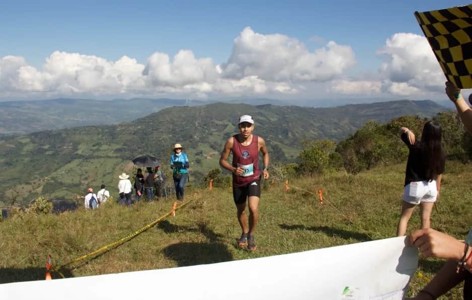 Runner reaching the finish tape on the summit, with a checkered flag and mountains behind
