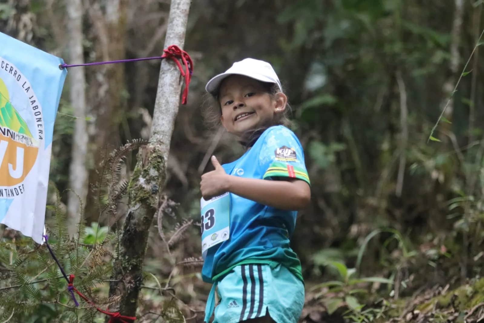Young runner smiling and giving a thumbs up in the forest, next to a KVJ flag