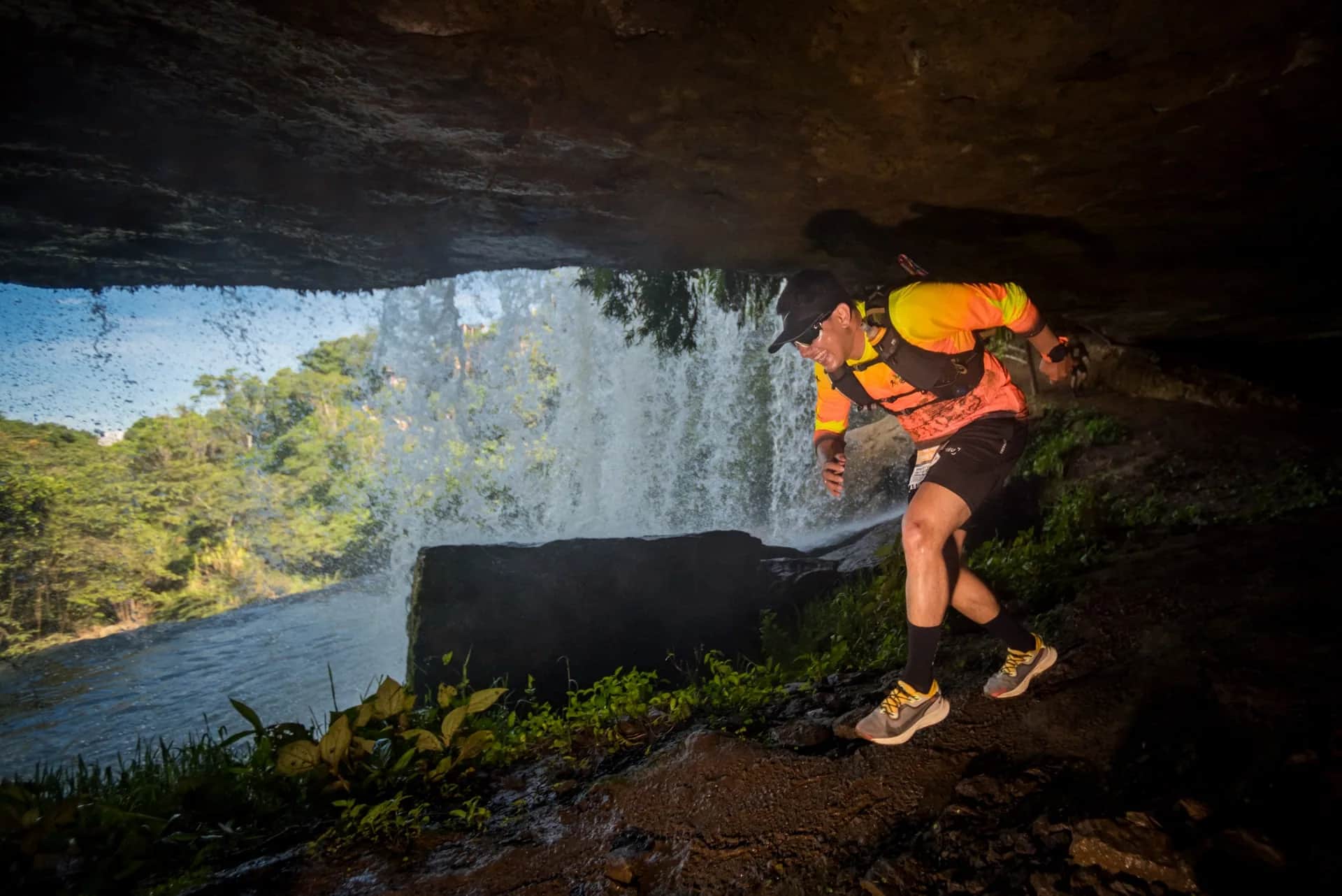 Runner passing under an overhanging rock, behind a waterfall