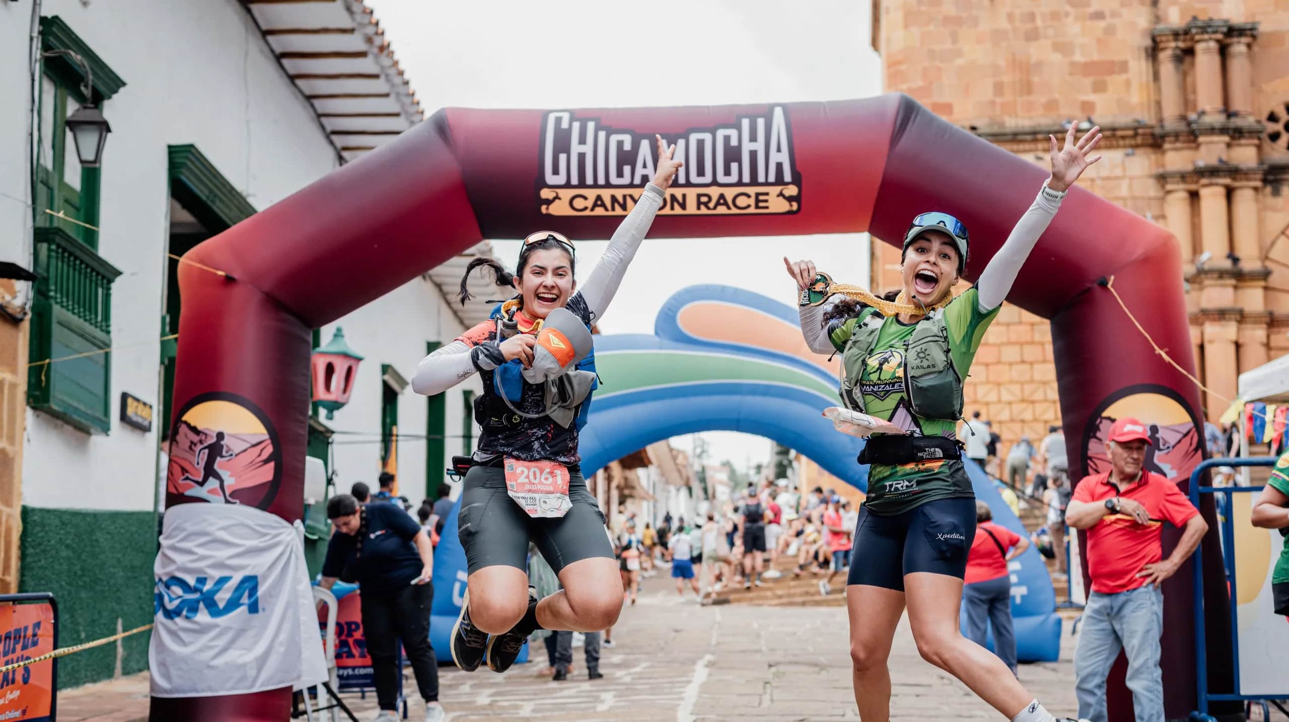 Two runners leap for joy under the finish arch in Barichara main square