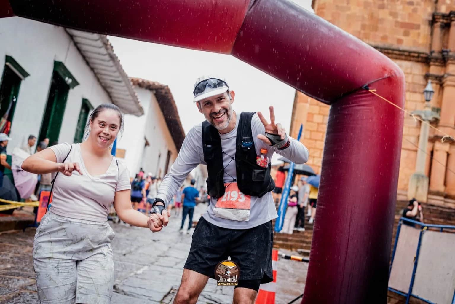 Two runners arrive hand in hand under the arch on a cobbled street in Barichara