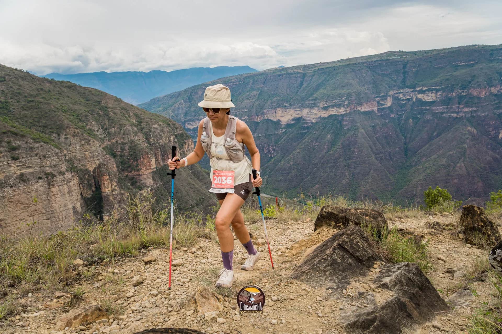 Runner in a hat with poles moving along the canyon rim