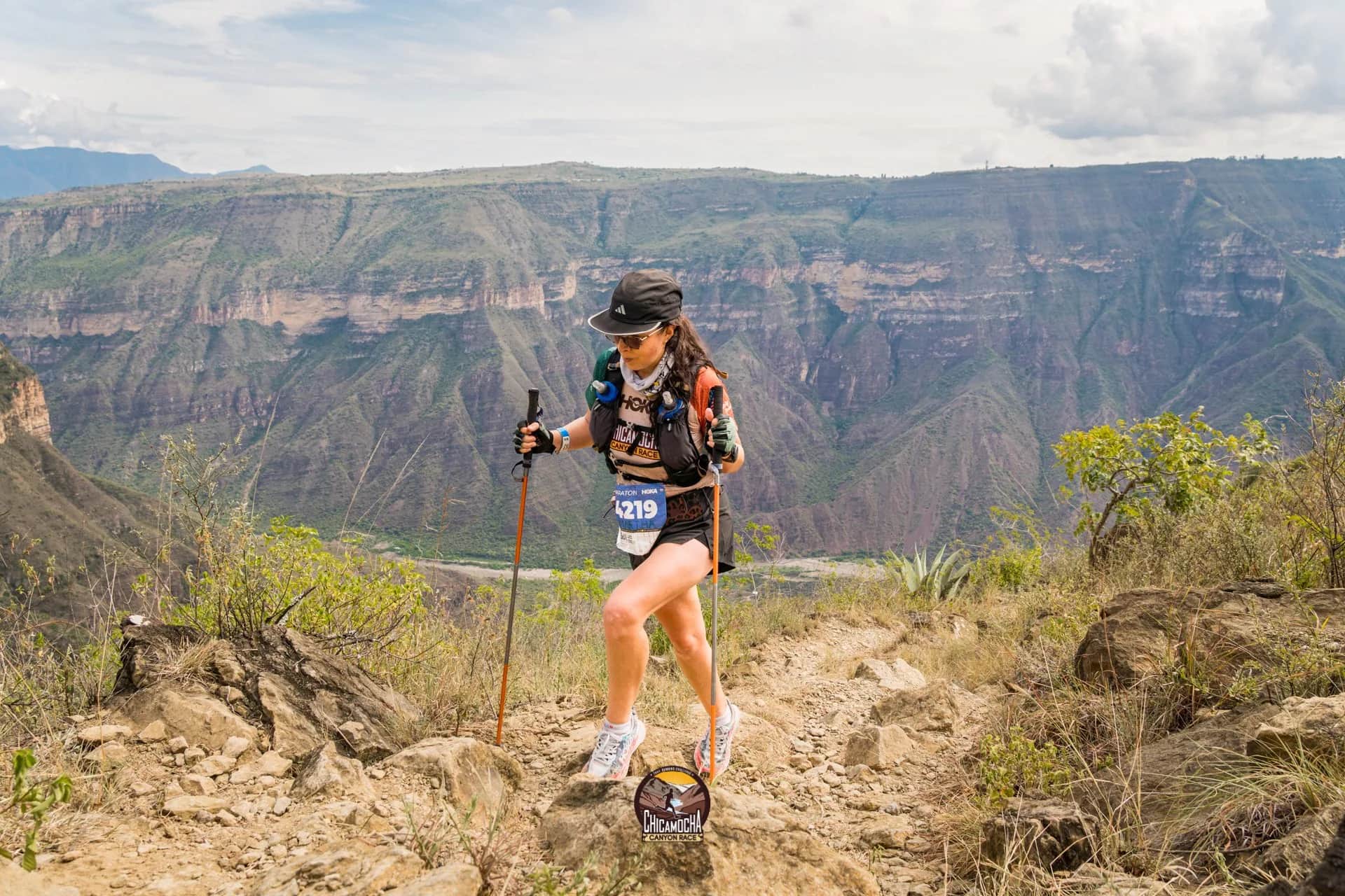 Runner with poles and bib on a rocky trail with the canyon behind