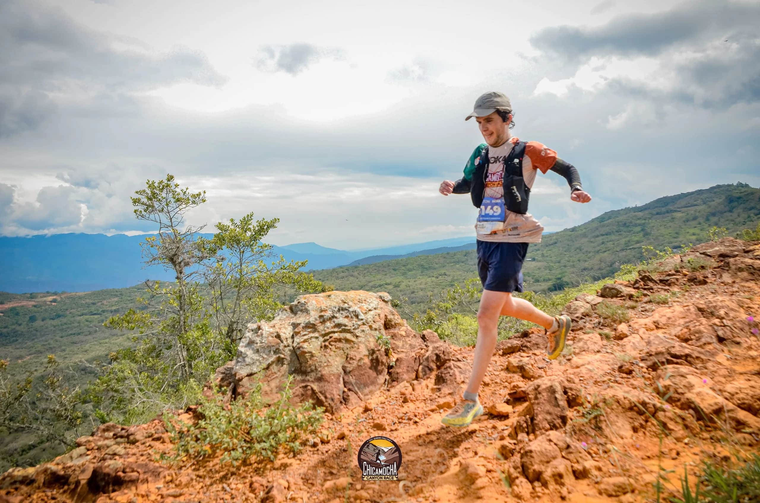 Runner bounding over red-earth rocks, with the valley and mountains behind