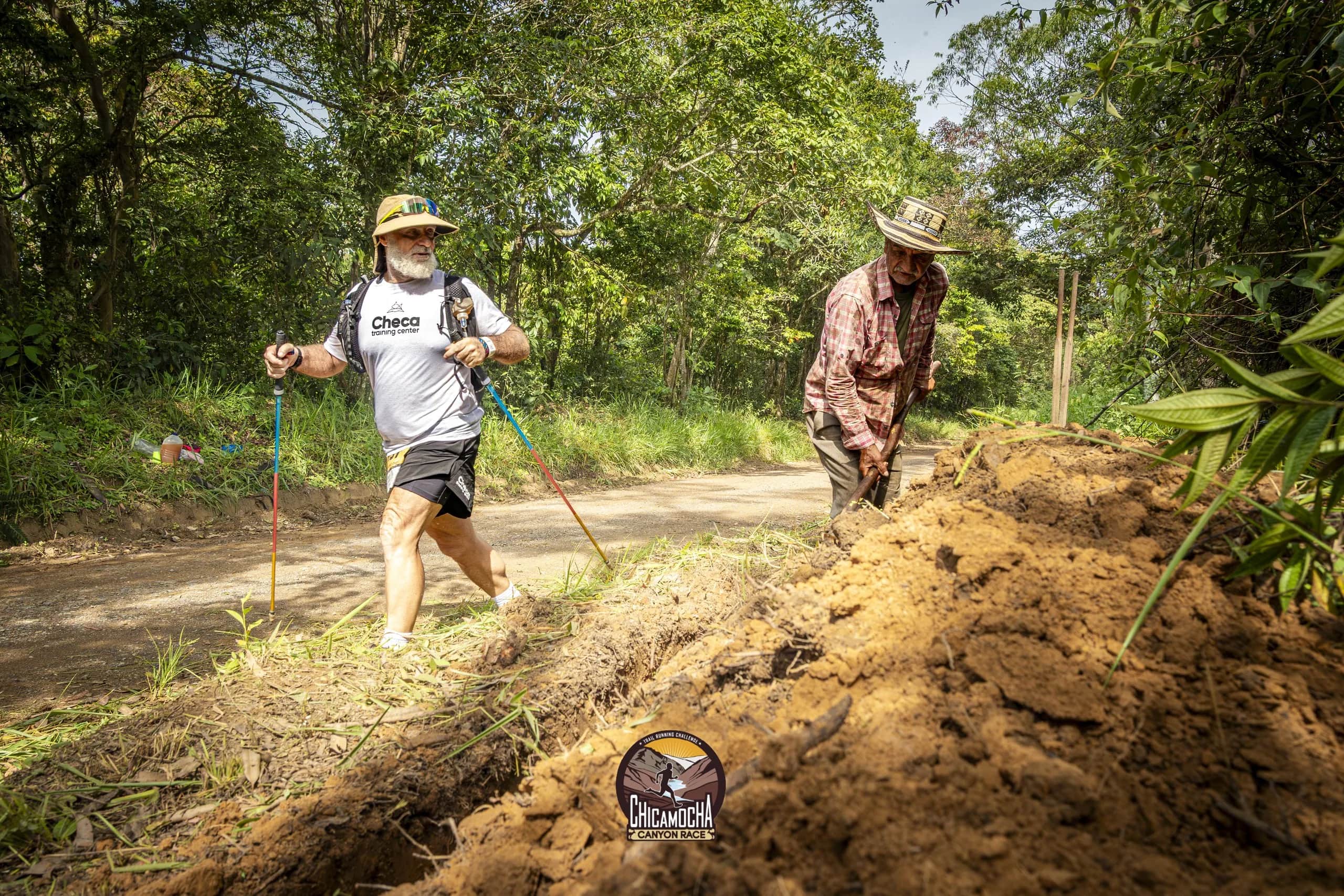 Corredor con sombrero y bastones pasa junto a un campesino que trabaja la tierra al lado del camino
